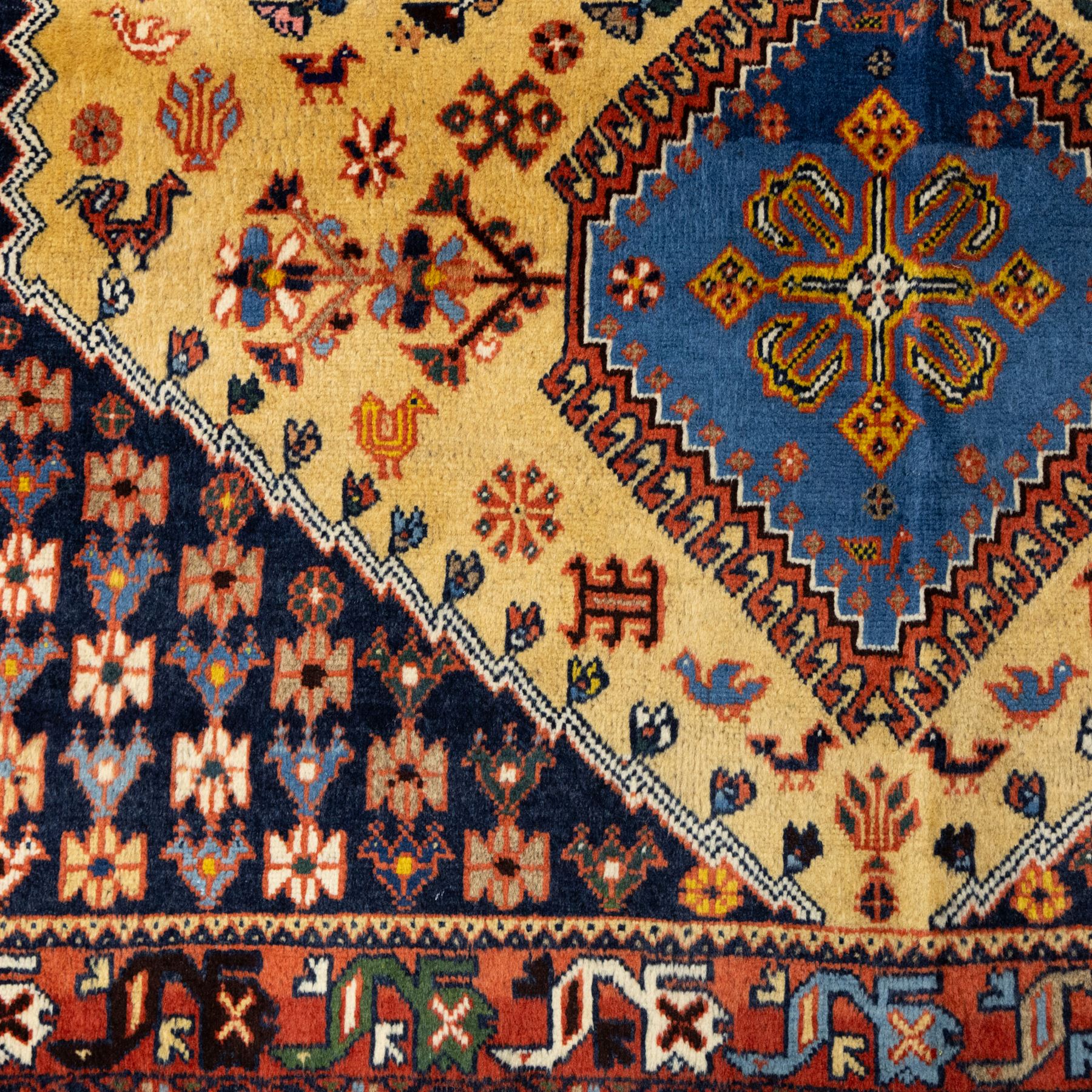 South Persian Yallameh hand-knotted rug, ivory ground, with a central stepped pole medallion design in blue and terracotta tones, surrounded by geometric tribal motifs incorporating stylised flowerheads, birds, hooked devices and angular vine work, enclosed by dark navy spandrels and a terracotta border with repeating geometric motifs, flanked by narrow patterned guard stripes, with cotton fringes