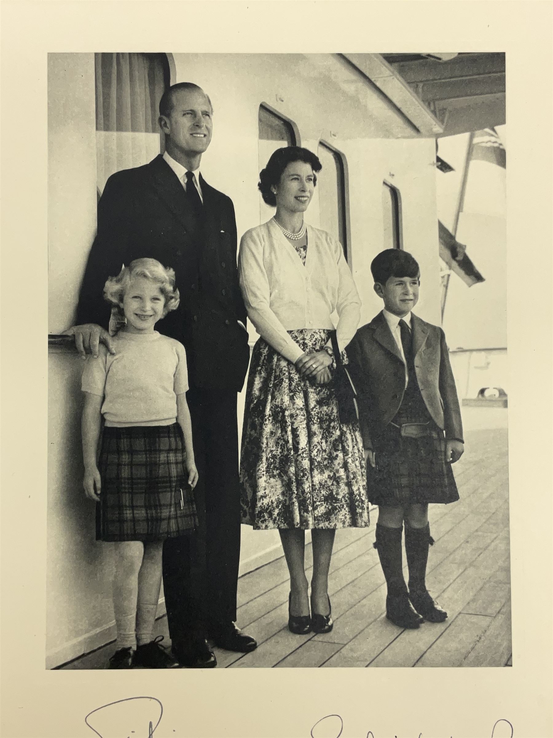 HM Queen Elizabeth II and HRH The Duke of Edinburgh - signed 1956 Christmas card with gilt embossed crown to cover, black and white photograph of the smiling Royal Couple with Prince Charles and Princess Anne on board Britannia, signed in ink 'Philip 1956 Elizabeth R',