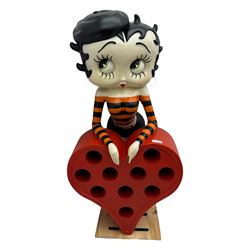 Contemporary large-scale Betty Boop painted wine rack, modelled leaning against a heart-shaped stand with ten circular bottle slots, dressed in black and orange striped attire