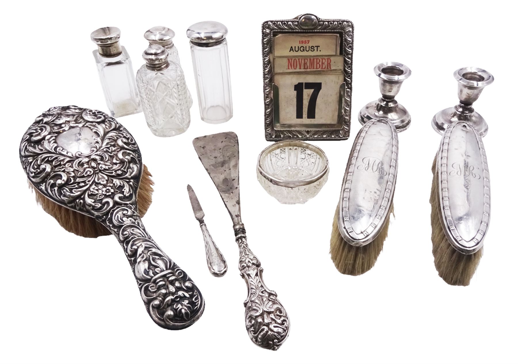 Group of silver, comprising Victorian silver mounted perpetual calendar with various date cards, hallmarked Henry Matthews, Birmingham 1900, silver mounted dressing table items, to include hair brush, with embossed decoration, pair of clothes brushes, and a shoe horn, together with a pair of silver mounted dwarf candlesticks, four cut glass jars/scent bottles with silver covers and a cut glass open salt with silver collar, all hallmarked 