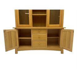 Light oak wall display cabinet, fitted with two glazed doors enclosing illuminated cupboards, above three drawers and two cupboards