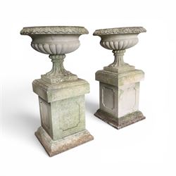Pair of weathered cast stone Neoclassical design garden Kylix shape urns, foliate moulded rim over a gadrooned underbelly, the scalloped socle over a rectangular pedestal with faux-panelled sides, stamped with stylised ‘H’ monogram