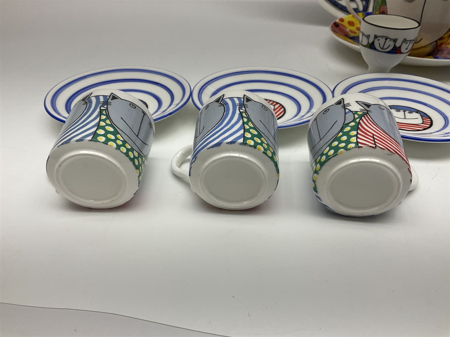 Modern studio pottery by Josie Firmin, to include cup and saucer, three espresso cups and saucers, pair of egg cups etc, each hand painted with varying cartoon cat designs