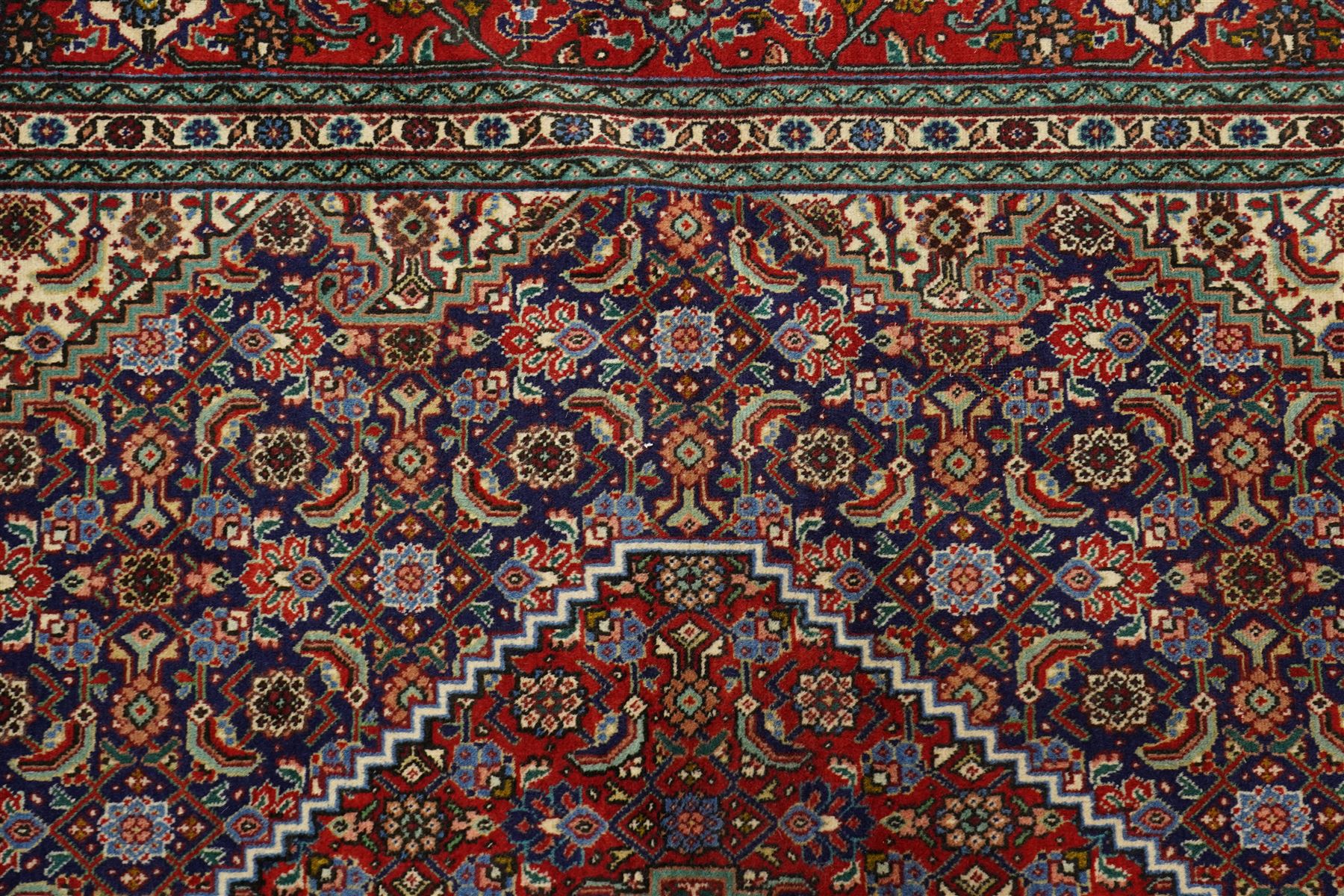 North West Persian Tabriz hand-knotted rug, ivory field with a central lozenge medallion in deep indigo and madder red, enclosing a inner reserve with stylized floral motifs, spandrels with angular floral sprays, main border of repeating floral vinery and palmettes, framed by multiple guard borders, with cotton fringe ends