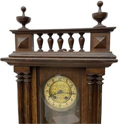 A German spring driven wall clock c1890, in a mahogany case with a glazed door, twin pilasters to the front and a balustrade gallery to the pediment, two-part dial with a repousse gilt centre and enamel chapter, Roman numerals and pierced steel hands, with an embossed gridiron pendulum and beat plate, eight-day spring driven movement striking the hours on a coiled gong.  With Key. 

