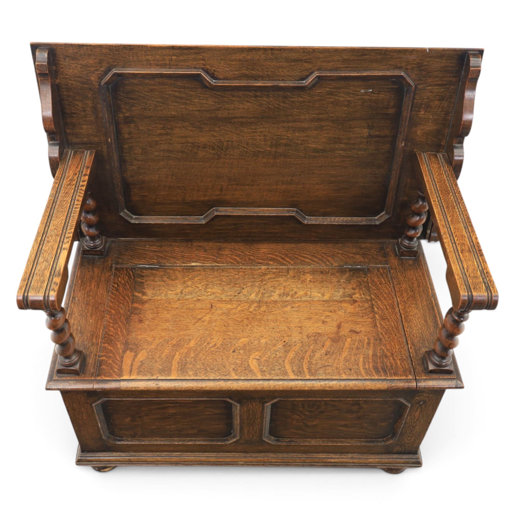 Early 20th century oak monks bench, panelled back converting to a table top, reeded armrests with barley twist uprights, hinged seat over panelled base supported on bun feet