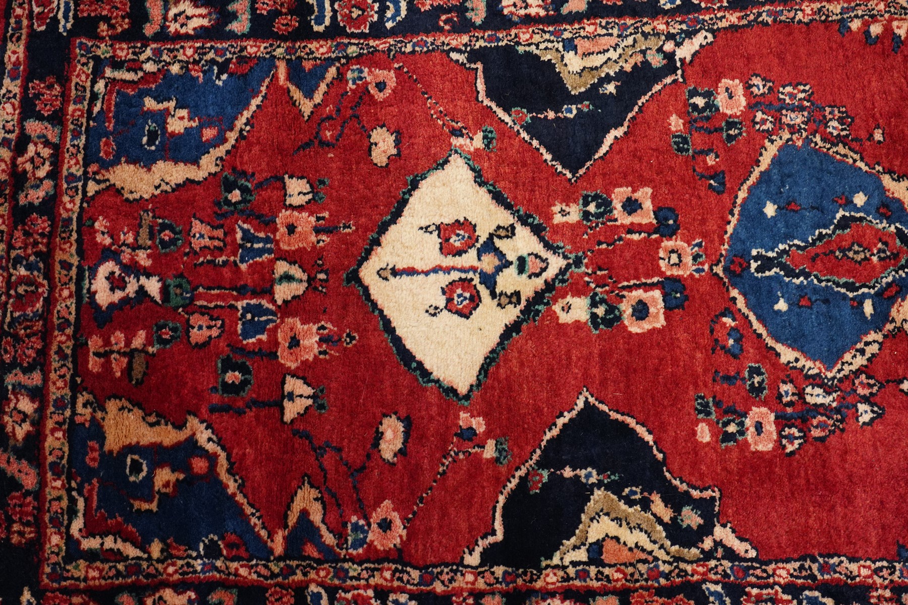 Persian Hamadan runner rug, the vermilion ground decorated with a row of ivory and indigo medallions interspersed with stylised flowering plants, indigo spandrels, enclosed by an indigo floral border and narrow patterned guard stripes
