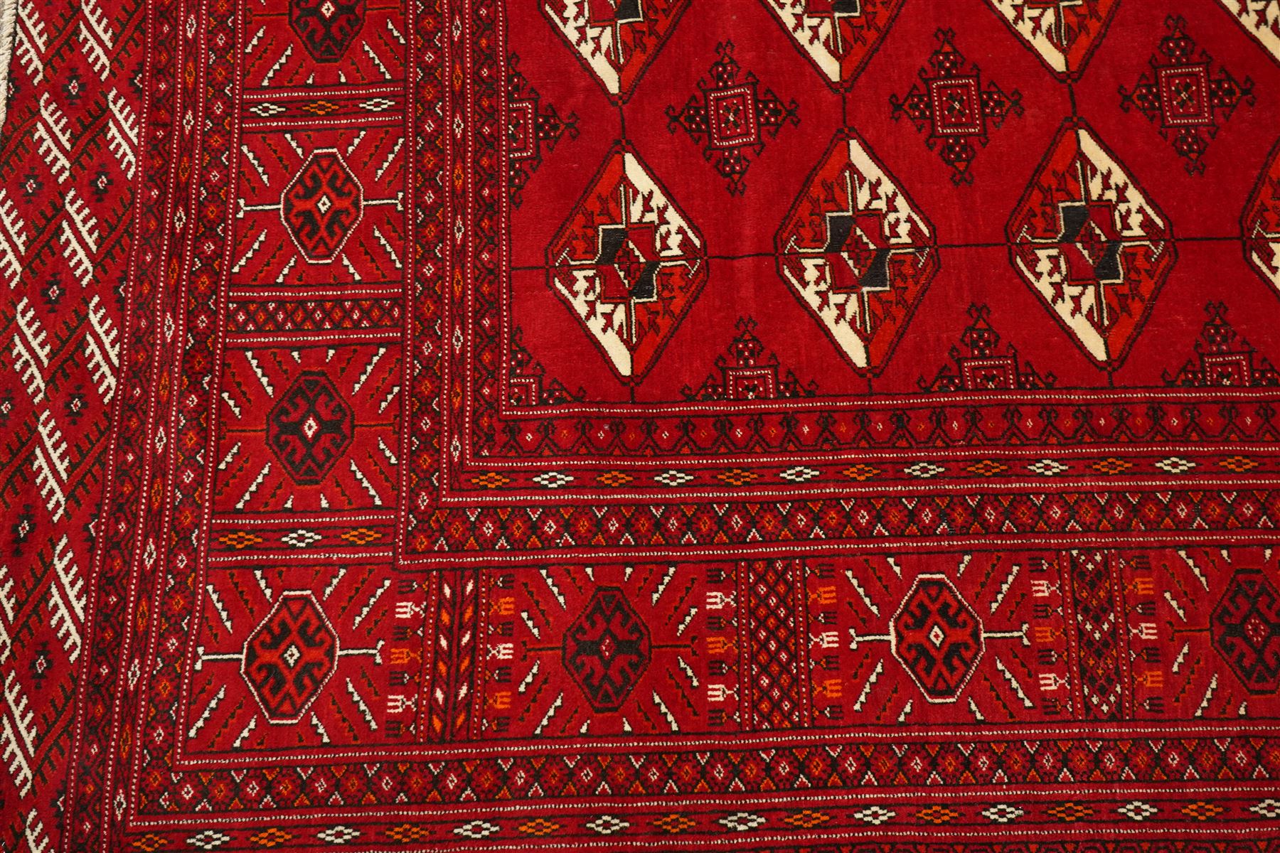 Turkmen hand-knotted carpet, deep crimson ground field, with an all-over lattice of repeating diamond guls, each enclosing angular cruiform motifs, and stylized tribal devices, interspersed with smaller geometric ornaments, main border decorated with repeating geometric motifs and stylized tribal elements, flanked by narrow guard stripes, with cotton fringe ends 