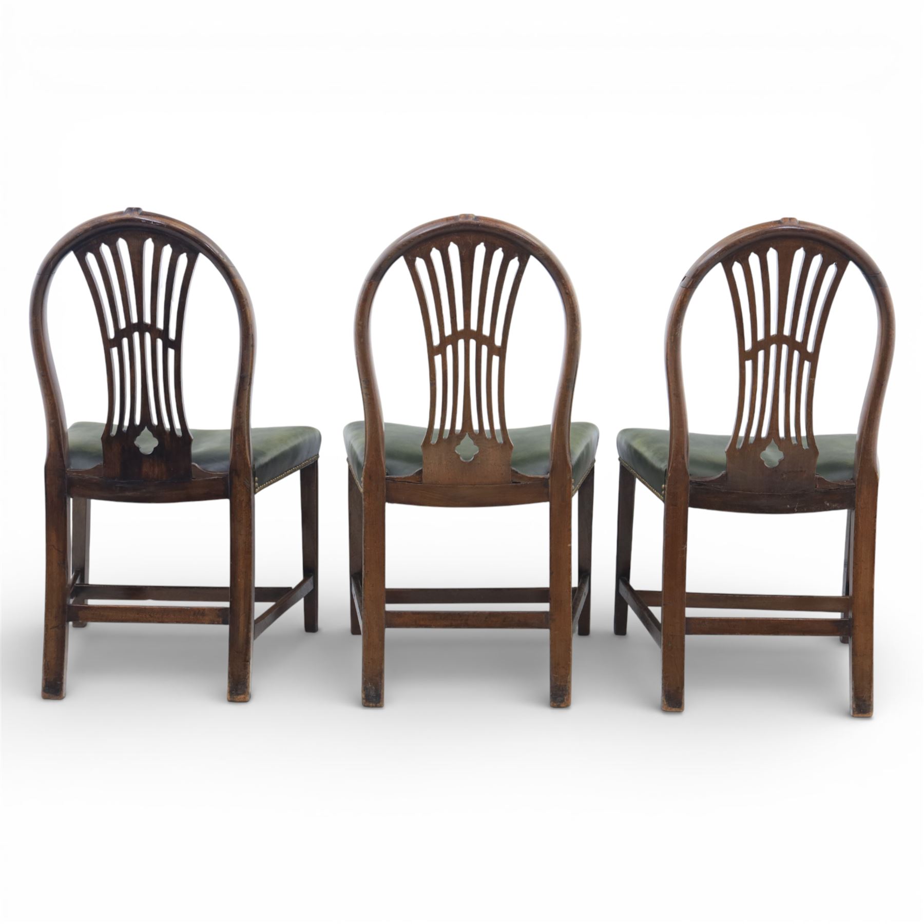 George III style set of six mahogany dining chairs, the arched backs with pierced and carved vase splats beneath carved husk and patera detail, drop-in upholstered seats covered in green leather with brass studded edging, raised on square section legs united by plain stretchers