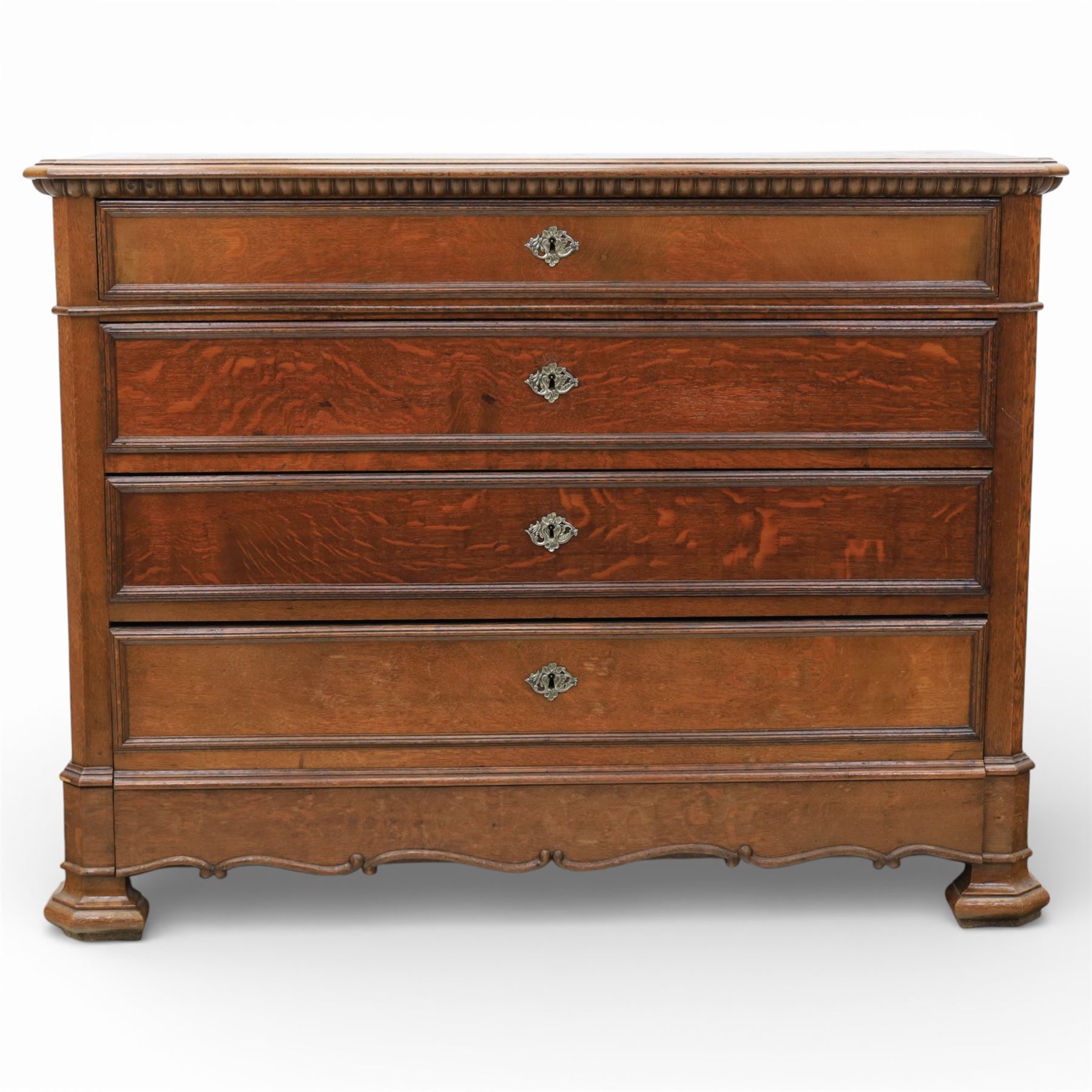 Late 19th century French provincial oak chest of drawers, moulded rectangular top with carved rope edge over four graduated long drawers with raised and fielded panels and ornate cast handles, canted angles and shaped apron below, standing on moulded block feet,