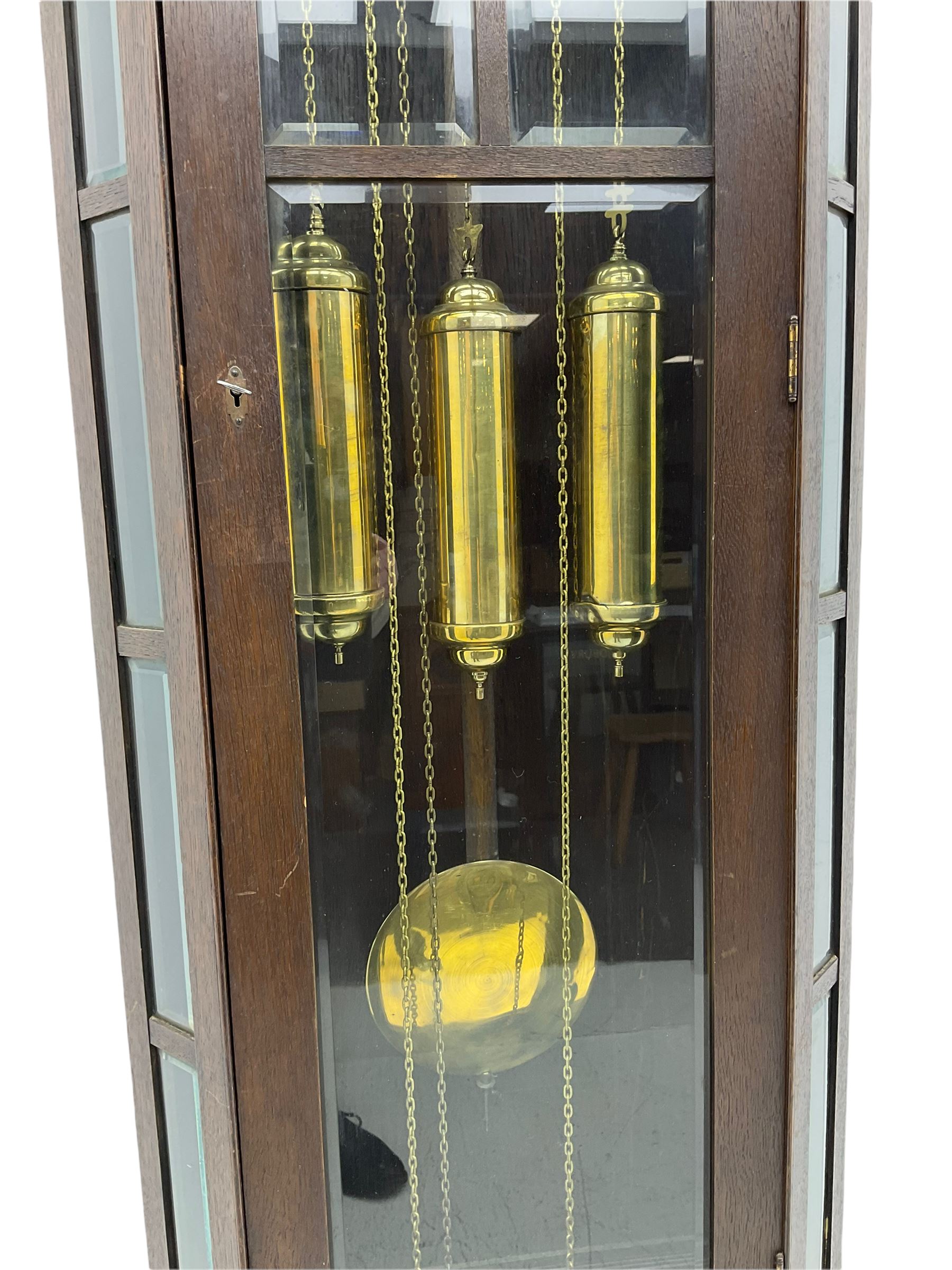 A mid-20th century weight driven floor standing clock in an oak case with canted glazed panels, full length glazed trunk door on a rectangular plinth with applied double skirting, white enamel dial with a gilt slip, upright Arabic’ numerals, minute markers, quarter hour Arabic’s and steel spade hands, with a three-train weight driven Westminster chiming movement chiming on two sets of gong rods.
With pendulum and weights.

