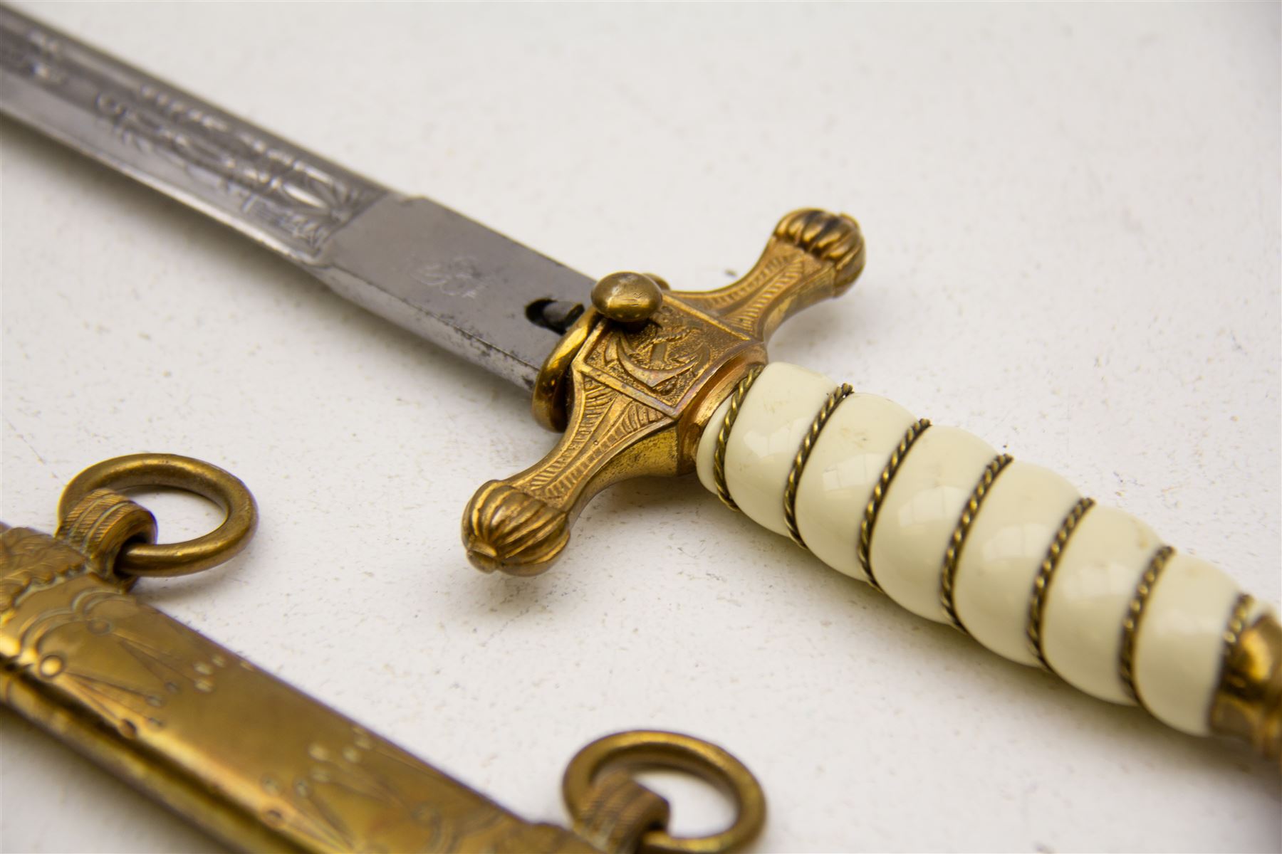WWII period German Kriegsmarine navel officers dress dagger by Carl Eickhorn, Solingen, with gilded pommel and cross guard with press stud release button, white celluloid grip with wire binding, housed in its original brass scabbard with two hanging rings, the etched double edged blade with Carl Eickhorn, Solingen makers trademark to the base, L39cm