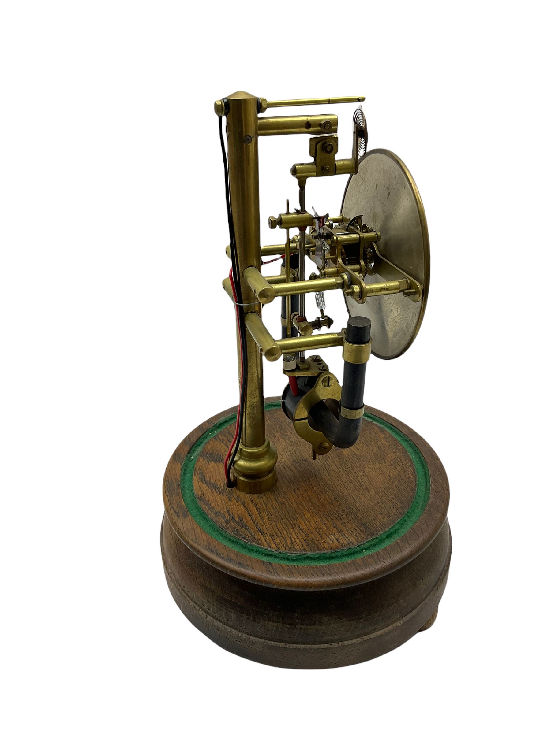 A 1920’s French 800-day Bulle electric battery clock on a turned wooden base, with a circular silvered dial with Arabic numerals, minute track and steel spade hands, skeletonised brass movement and escapement, the magnetic pendulum action is activated by the battery power source located in the base of the clock. No Dome.