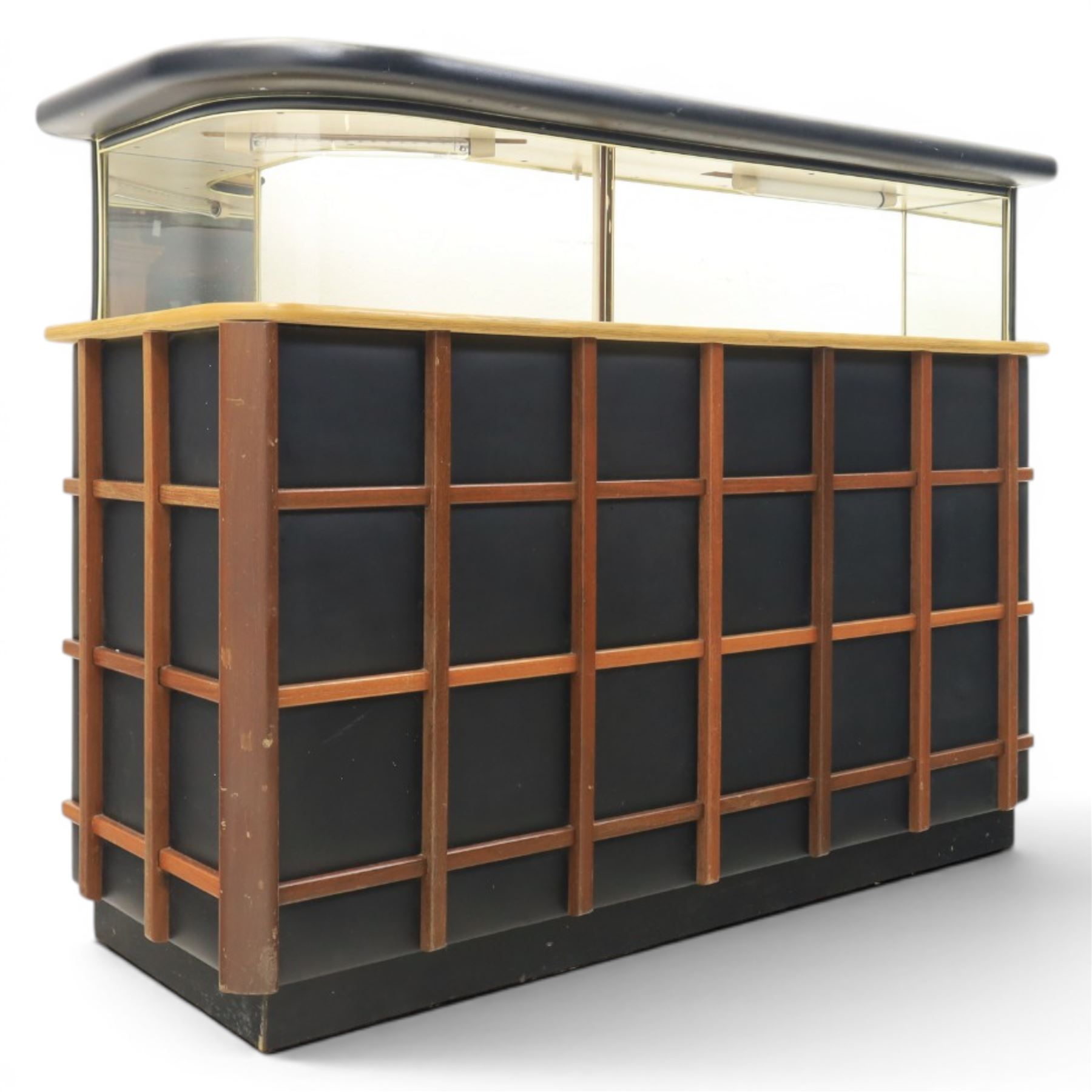 Barget of London - Mid 20th century L-shaped teak and black vinyl cocktail bar, shaped top with gilt metal banding and black cushioned edge over glazed upper section and open serving shelf, the reverse fitted with shelves, the front with applied lattice mouldings over black vinyl, on plinth base