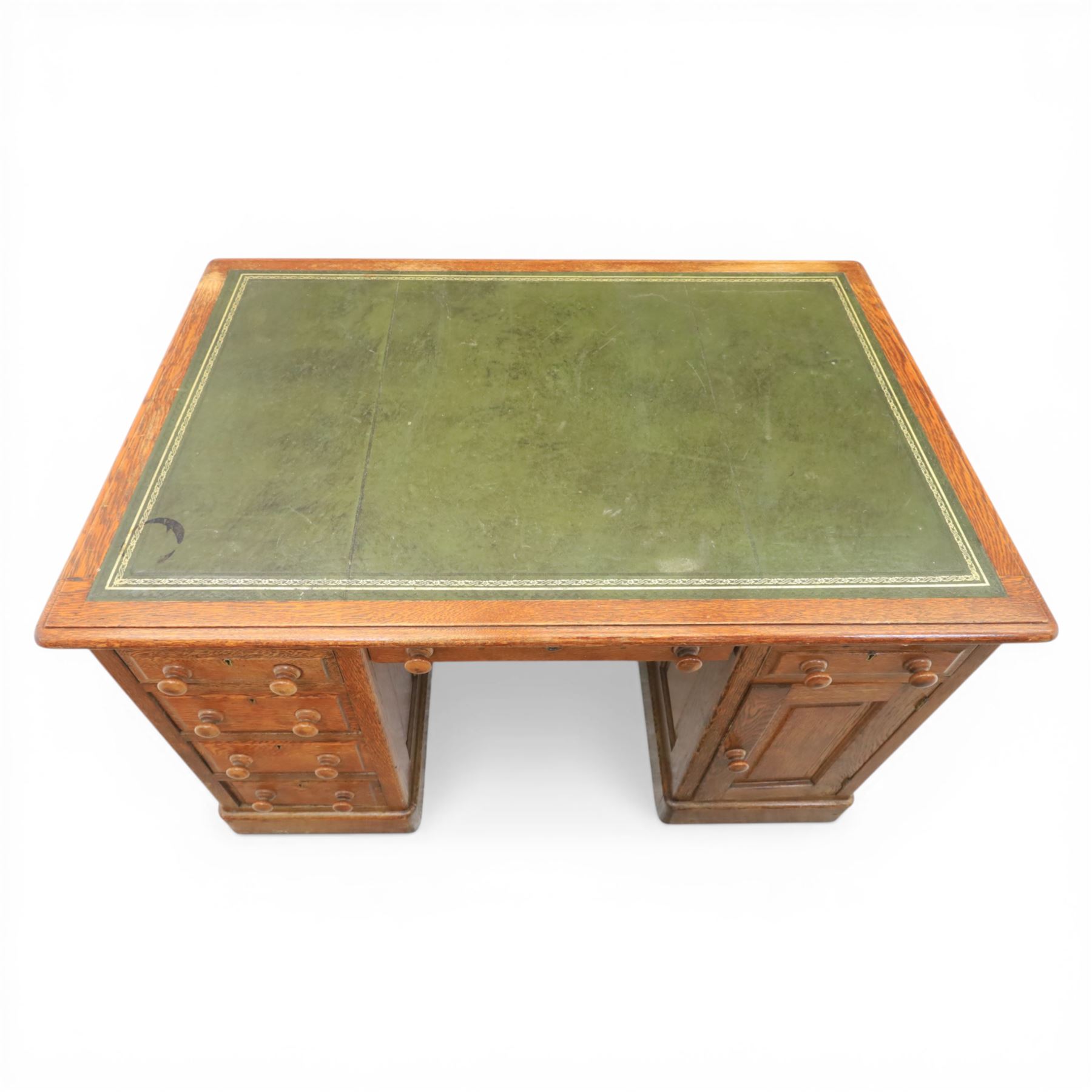 20th century oak compact pedestal desk, tooled green leather inset top, above a single frieze drawer, with a bank of four graduated drawers and a drawer and cupboard, panelled sides raised on castors