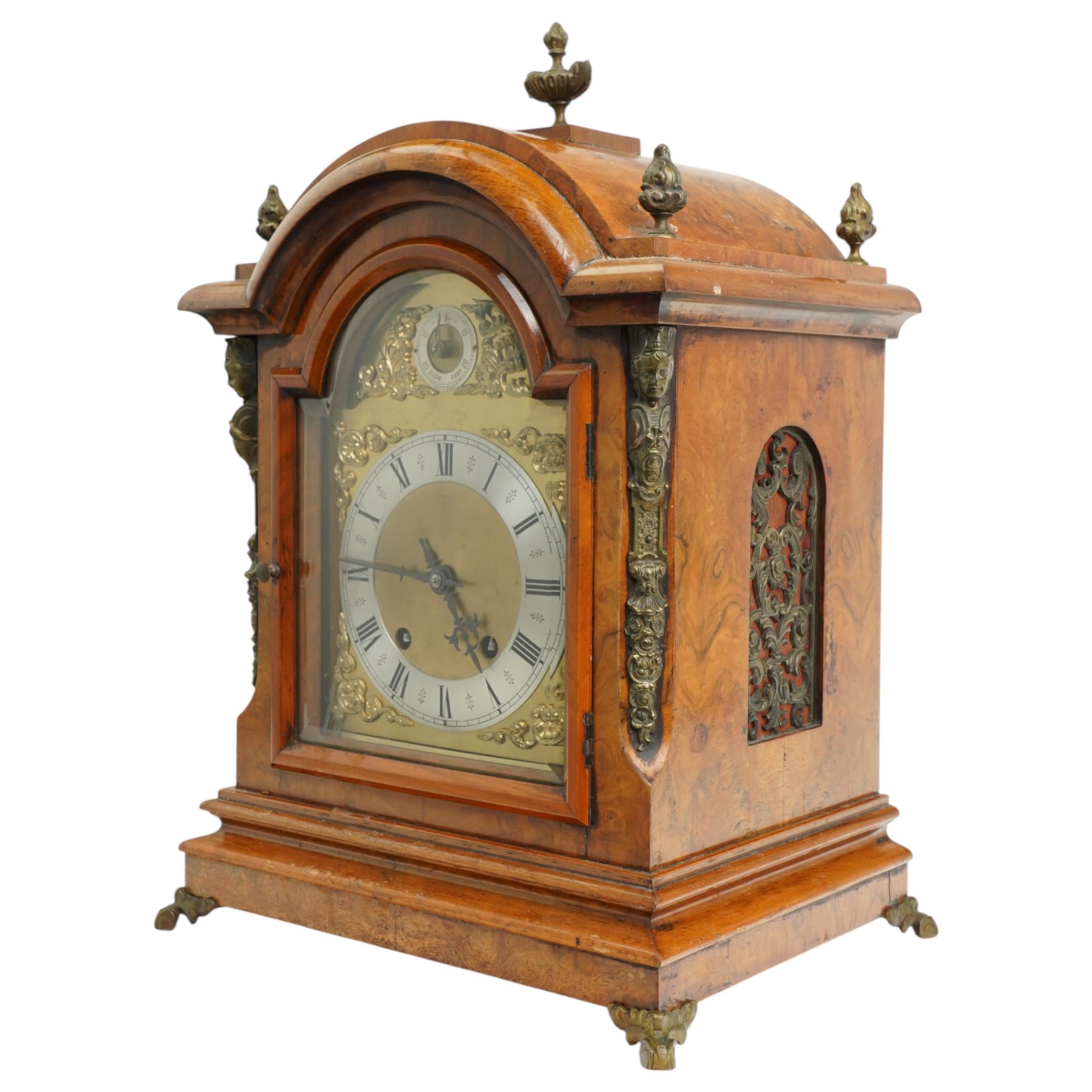 German-early 20th century mantle clock c1910, in a walnut case with a break arch top and decorative cast brass finials, brass silk backed sound frets to the sides and a glazed break-arch door flanked by a pair of cast brass caryatid, on a dee ogee moulded plinth and raised on splayed paw feet, brass dial with cast spandrels and a matted dial centre, silvered chapter ring with Roman numerals, gothic steel hands and a conforming pendulum regulation dial to the arch, two train going barrel movement with rack striking, sounding the quarters on two gongs and the hour on one, With Pendulum and key.
