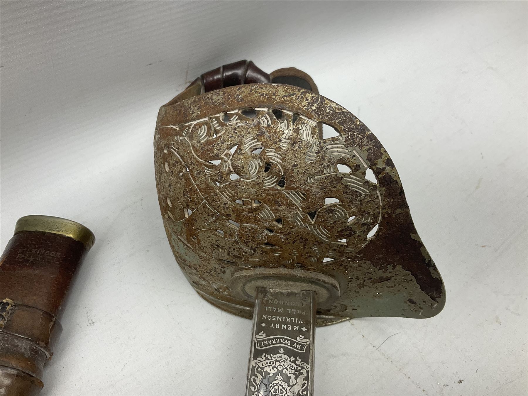 George V 1897 pattern Army Officer's sword by Henry Wilkinson Pall Mall London, the 82.5cm 'London Made' blade etched to both sides with Royal Crests and cyphers etc, pierced half-basket hilt with wire-bound fish skin grip and remains of leather knot strap; in leather covered field service scabbard L101cm overall; and two 14th Prince of Wales Own swagger sticks (3)