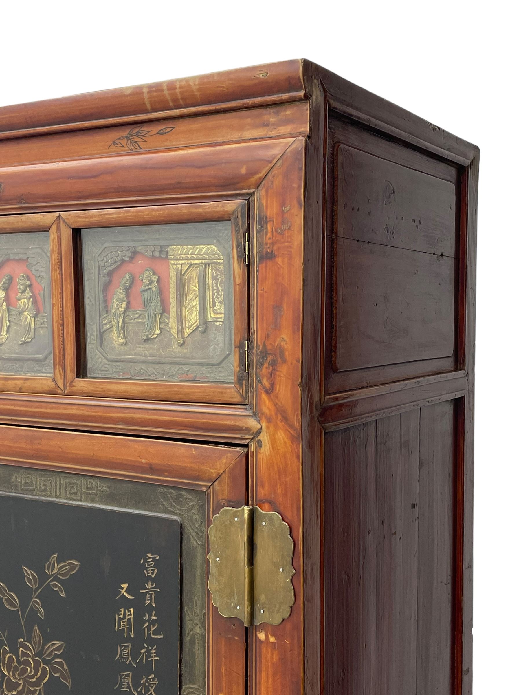 Late 19th century Chinese Qing dynasty red and black lacquered wood cabinet,  Fujianese province, upper cupboard enclosed by two doors with relief carved and gilt panels depicting figures behind glass, the large cupboard enclosed by two panelled doors carved with trailing foliate branches and birds, inscribed with Chinese characters, to the left ‘The red mountains are in the shape of Phoenixes and appear auspicious’ and to the right, ‘Wealth and honour are given by flowers and I hear the sound of the phoenix', fitted with two drawers, on square supports with carved brackets 