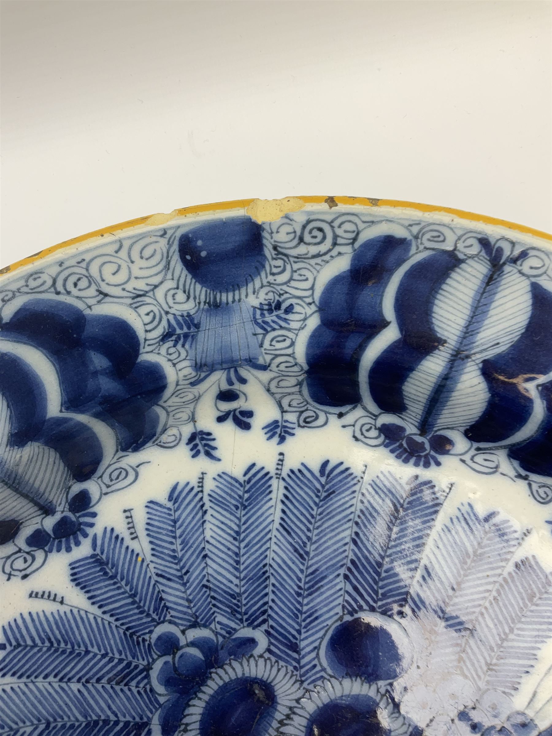 18th century Delft blue and white peacock pattern dish, painted with a fan of peacock feathers behind an urn of fruit and flowers, D34.5cm. 