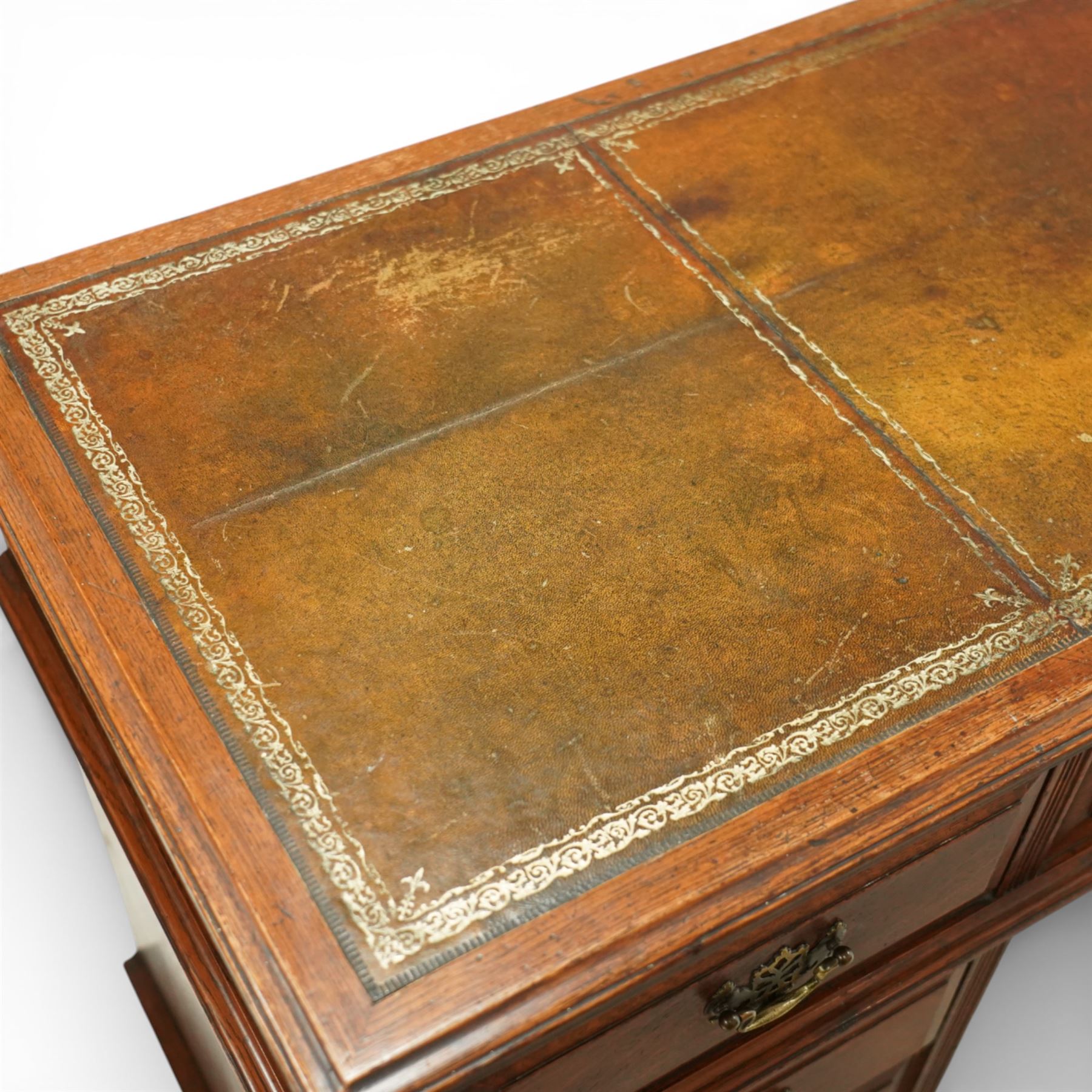 Late Victorian oak nine drawer desk, the rectangular top inset with a tooled leather writing surface bordered in gilt, above three frieze drawers and two pedestal cupboards each fitted with three graduated drawers, all with brass swan neck handles, raised on plinth bases