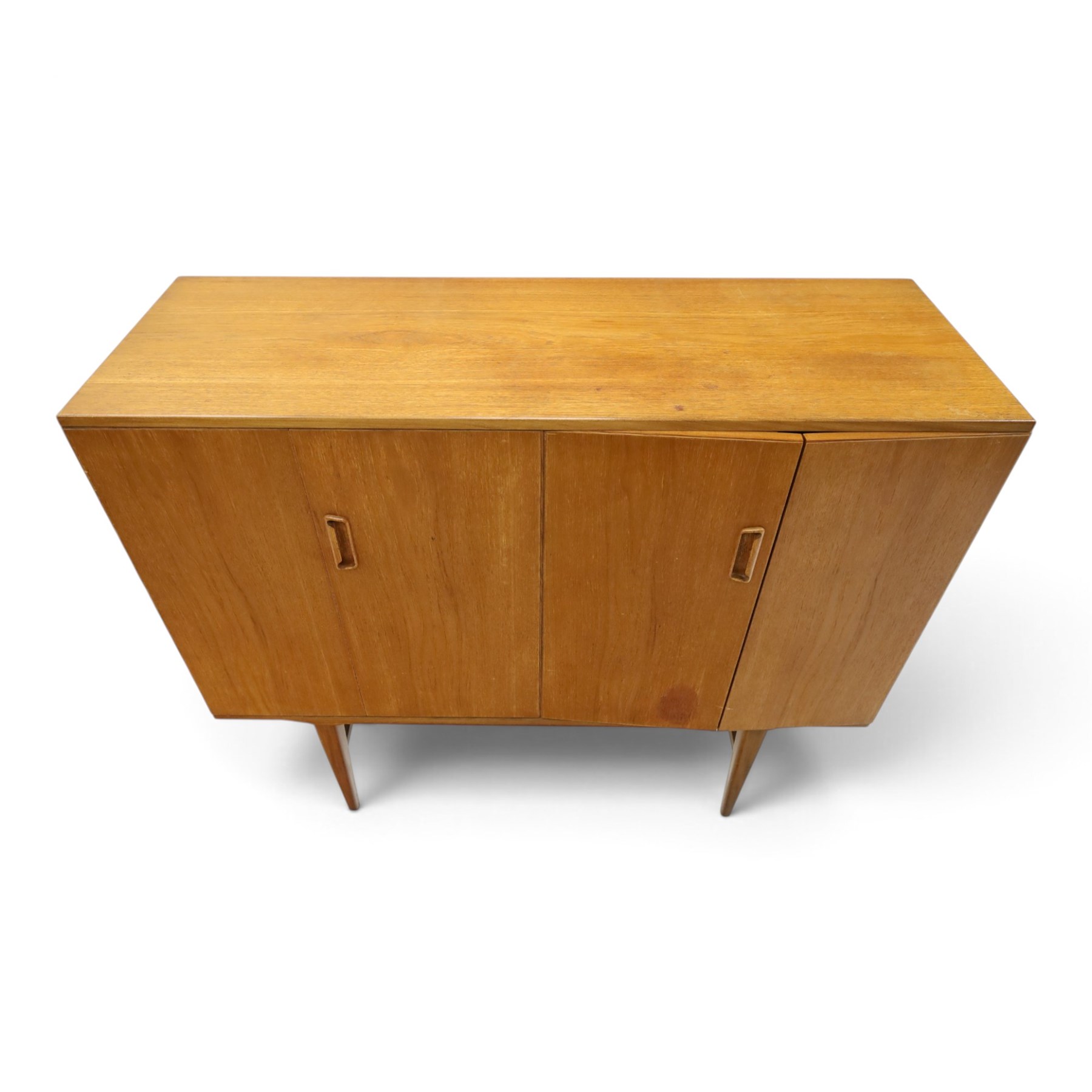 Alfred Cox - mid-20th century teak cabinet, rectangular top over two bifold doors with inset handles, opening to reveal three central graduating drawers surrounded by assorted shelves, raised on tapering supports united by H-stretcher, stamped to inside of drawer