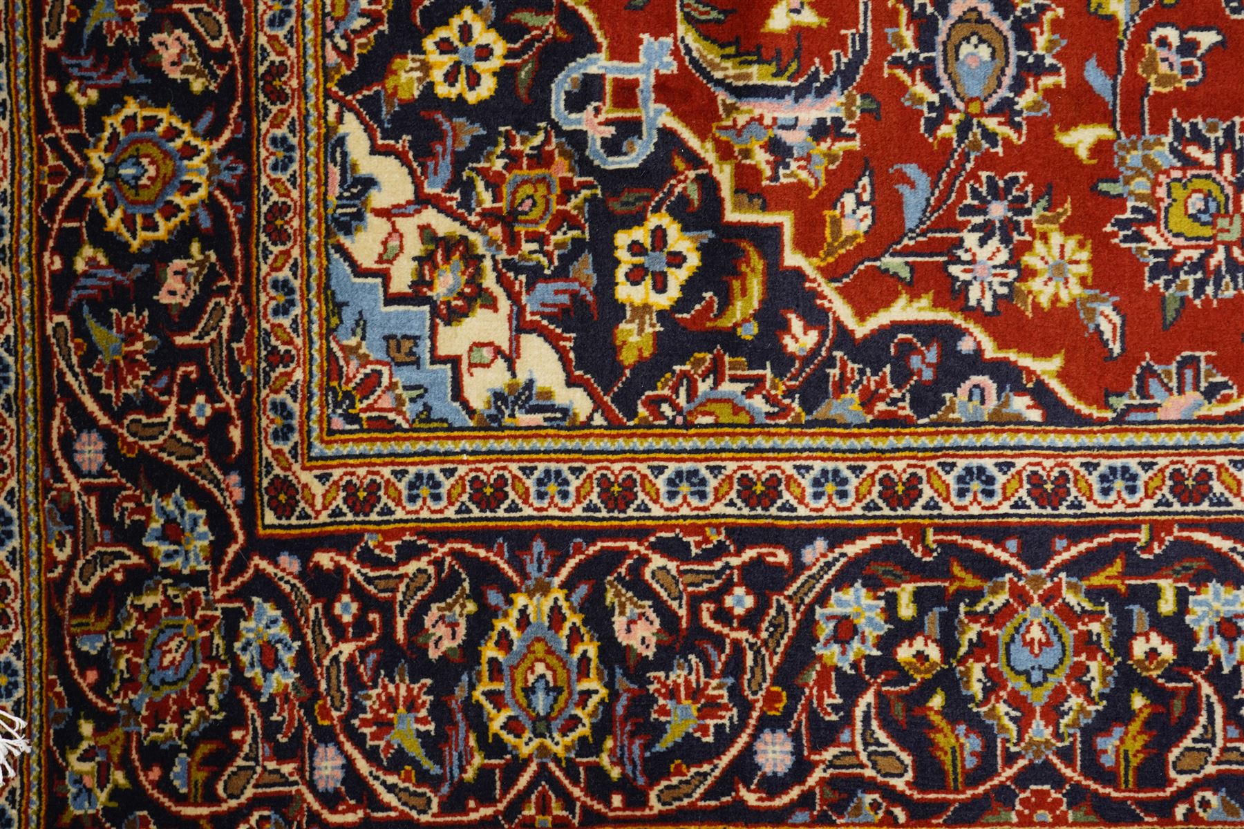 Central Persian Kashan hand-knotted rug, madder red field with central articulated cusped medallion in ivory and sky blue, issuing network of scrolling arabesques palmettes and floral sprays with conforming spandrels, indigo main border of scrolling vinery and stylized palmettes, framed by multiple guard borders, with cotton fringe ends  
