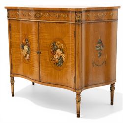 Sheraton Revival satinwood serpentine-front cabinet, the shaped cross-banded top with ebony stringing and painted scrolls of acanthi and ribbon work with a bell-flower border, the banded frieze painted with repeating acanthus scrolls, the matched veneer doors painted with oval panels of floral bouquets, raised on turned and tapering supports