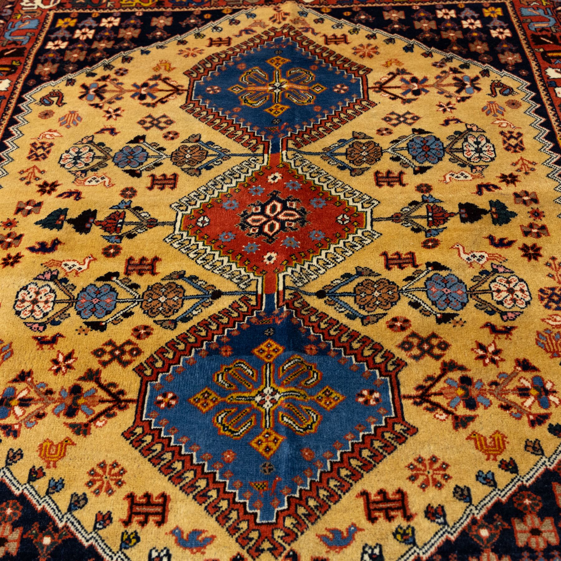 South Persian Yallameh hand-knotted rug, ivory ground, with a central stepped pole medallion design in blue and terracotta tones, surrounded by geometric tribal motifs incorporating stylised flowerheads, birds, hooked devices and angular vine work, enclosed by dark navy spandrels and a terracotta border with repeating geometric motifs, flanked by narrow patterned guard stripes, with cotton fringes