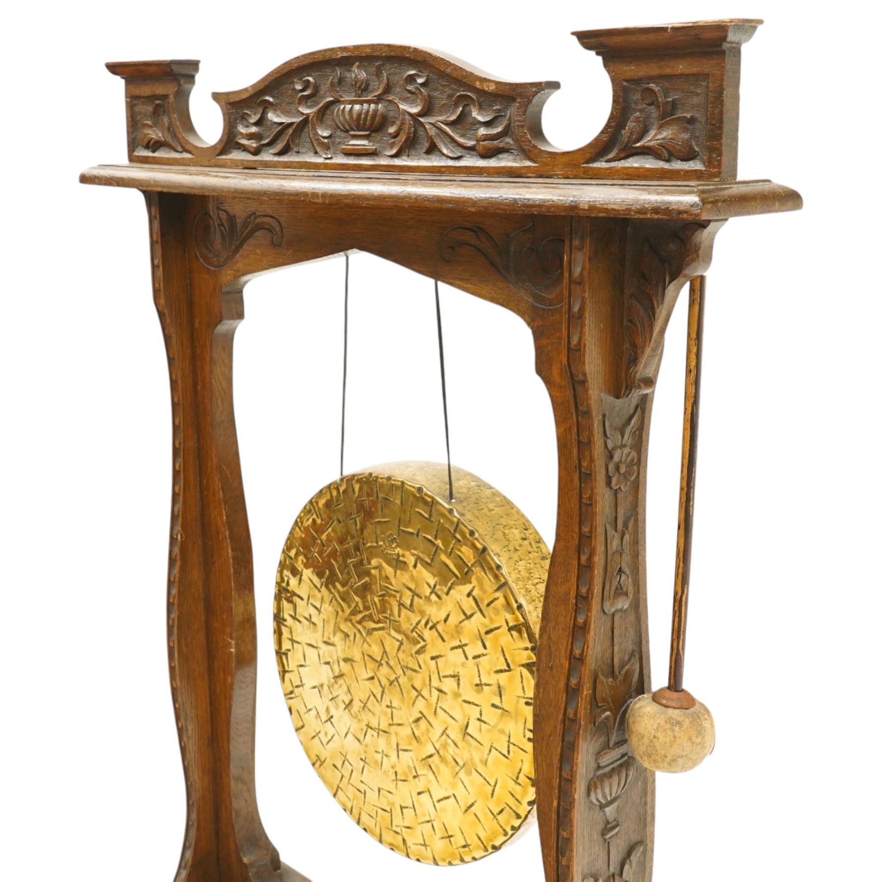 Late Victorian Arts & Crafts carved oak framed floor standing dinner gong, the cresting rail carved with central urn and trailing foliage, over shaped end supports decorated with graduating tulip and floral motifs, on rectangular base with scroll sledge feet, the brass gong stamped with William Suckling of Birmingham 'Burmese' makers mark, with striker