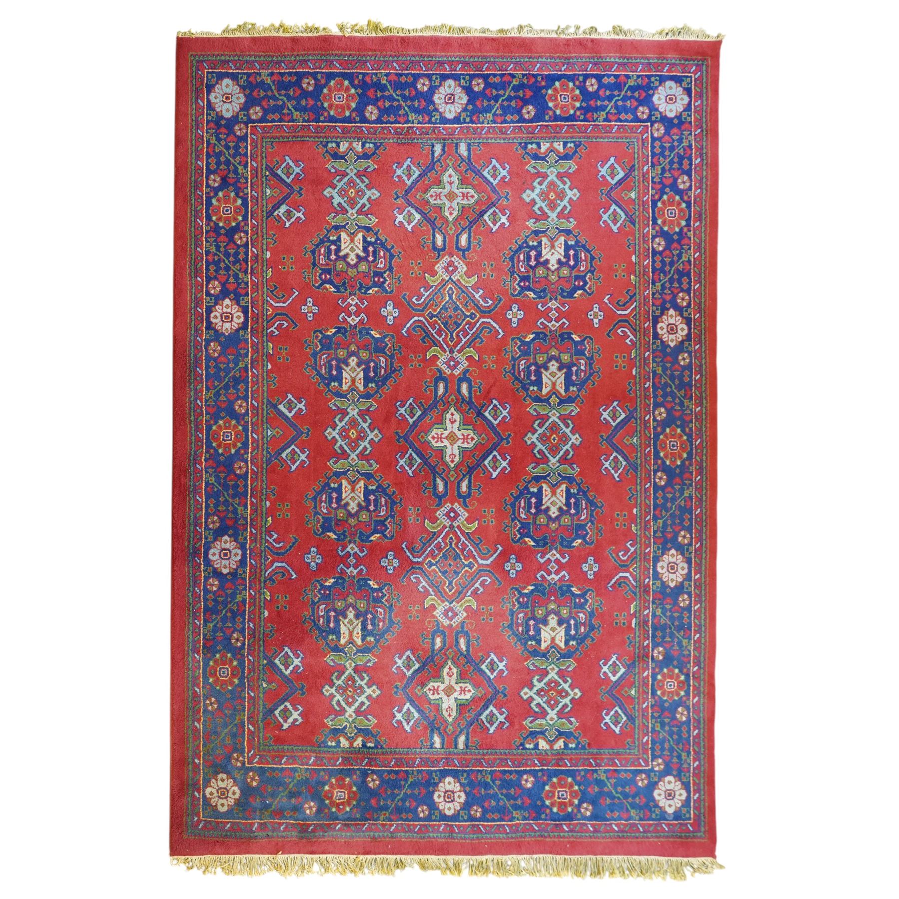 Indian Kayam rug, the rectangular field with repeating geometric medallions on a red ground, within a blue border of stylised floral motifs, with guard borders and fringe terminals