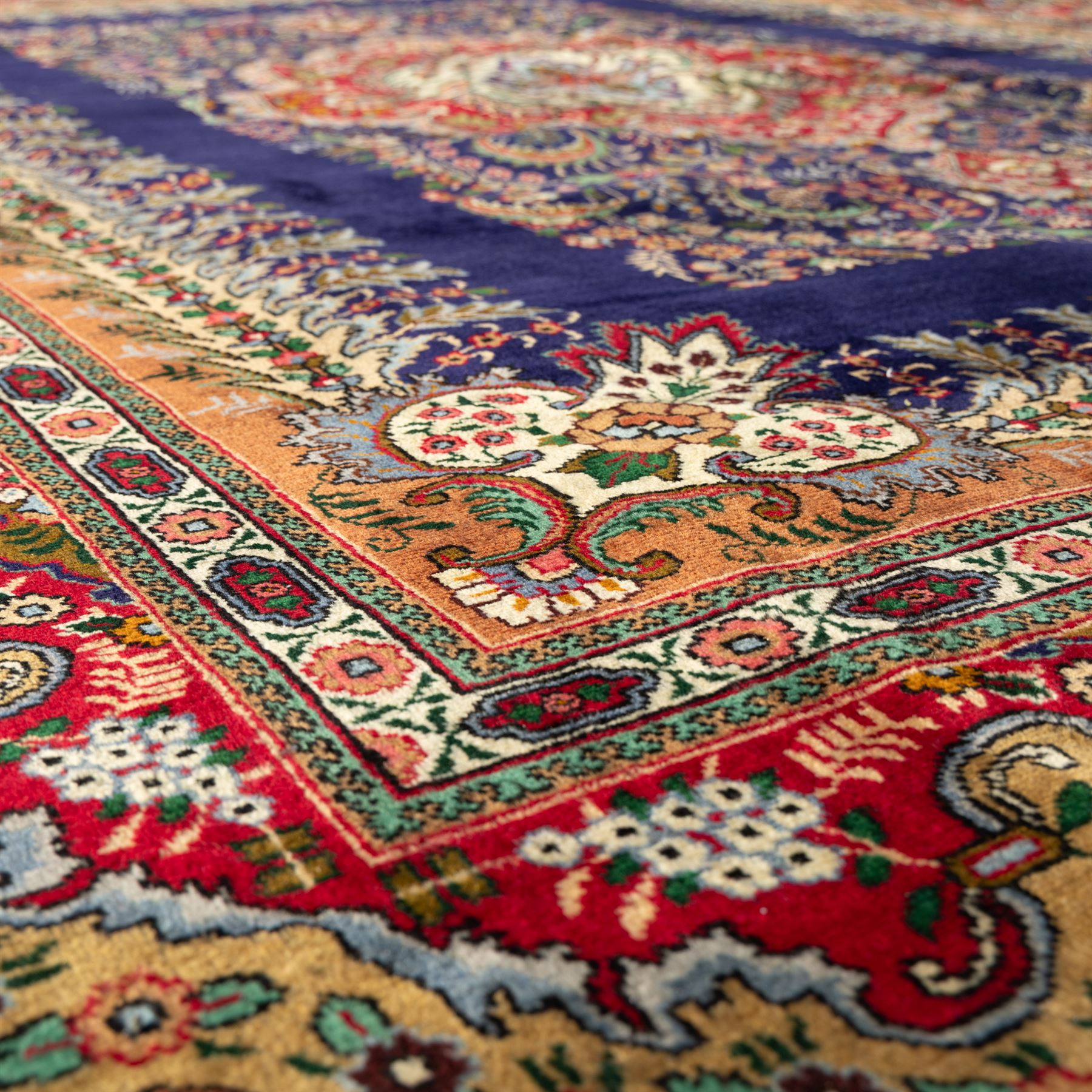 Persian Kashan rug, deep blue ground with central red and ivory lobed medallion framed by dense floral motifs, multiple borders with foliate and geometric design in red, blue and ivory, from the central Iran region