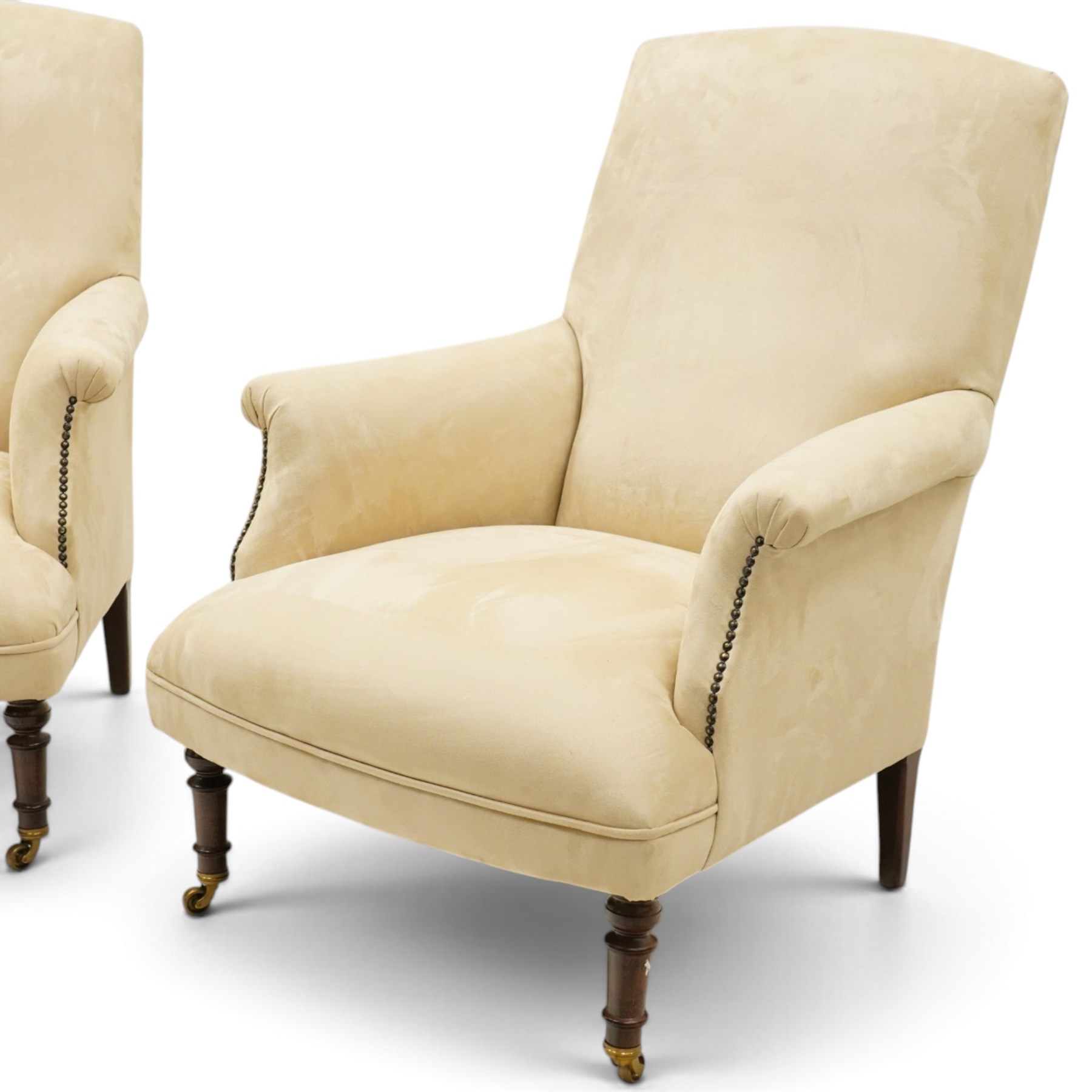 Sofas & Stuff - pair of ‘Thistle’ armchairs upholstered in neutral fabric, each with gently sloping back, padded scroll arms with close-set stud detailing, loose seat cushions, raised on turned wooden legs with brass castors