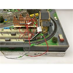 Table top 'N' gauge continental scenic layout as a split level town with various loops of track, station with numerous platforms, engine shed, assorted buildings, roads with motor vehicles and figures, tunnels, trees, river with bridge, tram depot etc 122 x 52cm