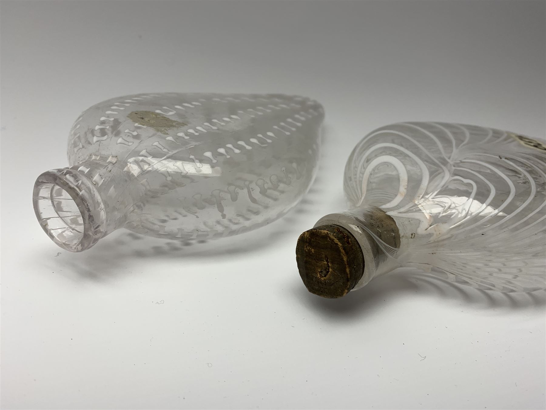 19th century Nailsea glass flask of compressed ovoid form, the clear body with opaque white combed decoration, H21cm, together with another similar example decorated with enamelled stylised bands, H23cm