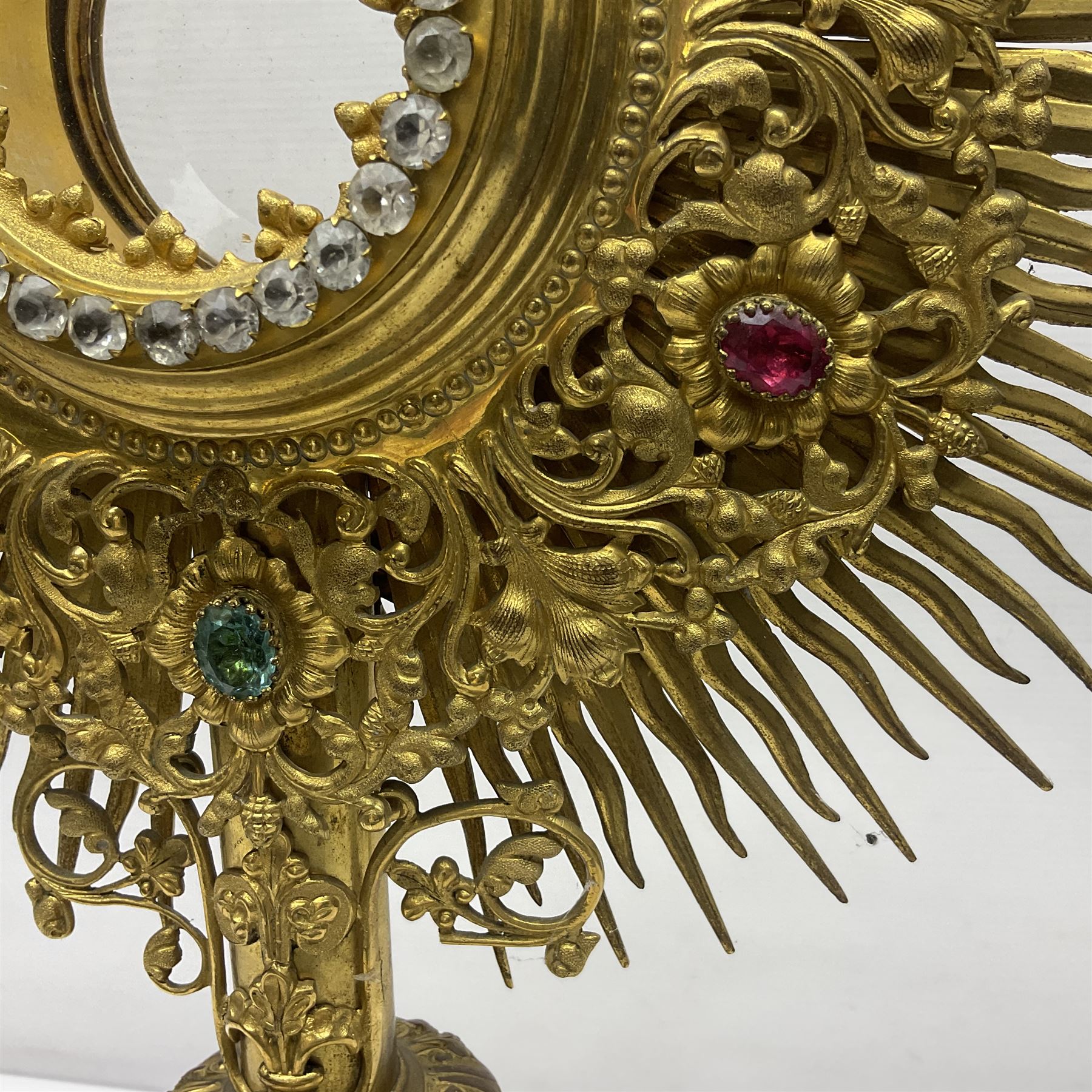 20th century gilt metal monstrance, in the Gothic revival style, with glazed aperture to centre surrounded with clear paste stones, in a pierced floral and scroll border set with coloured paste stones, within a sunburst surround, on a paste set knopped stem and similar foliate foot, H59.3cm