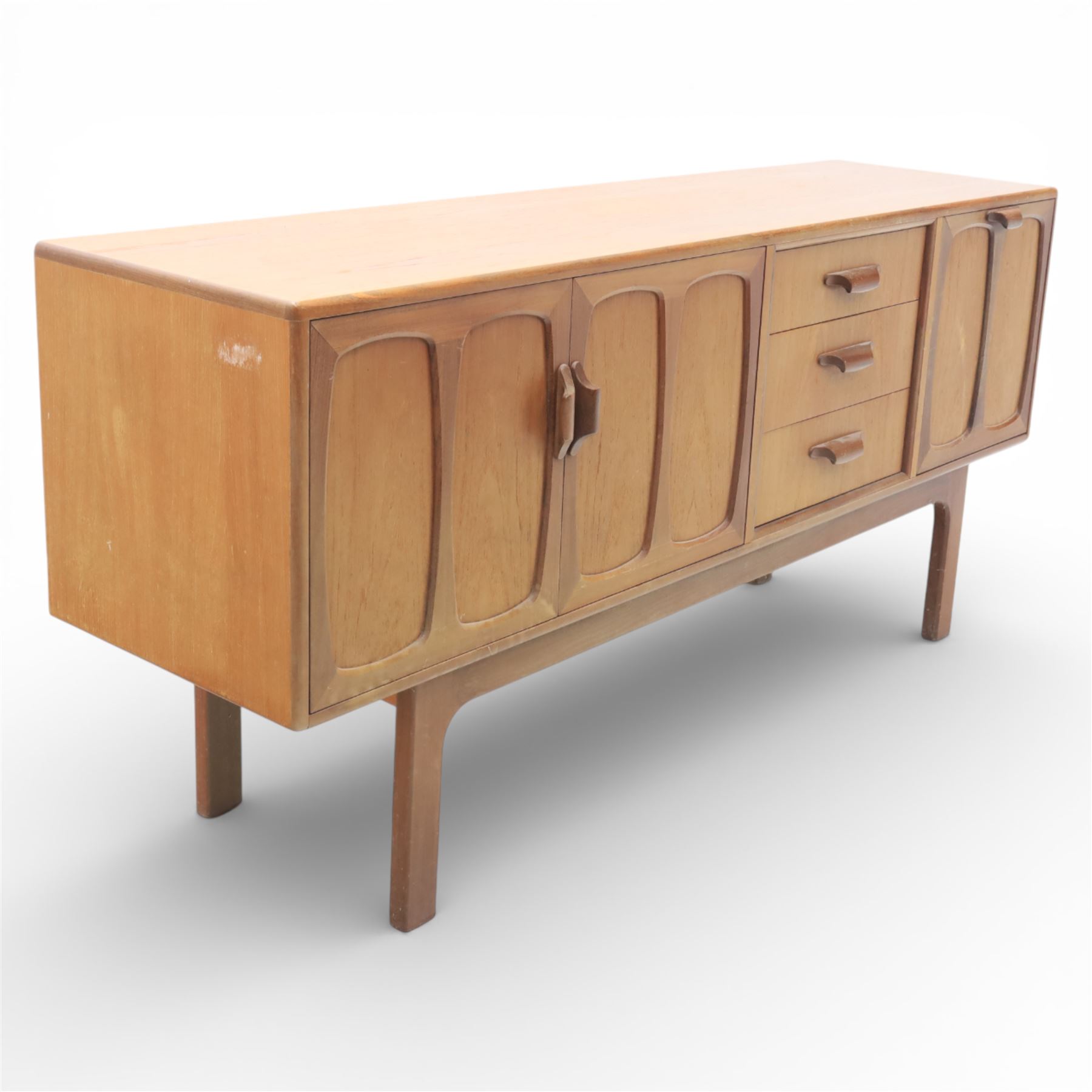 G-Plan - ‘Brasilia’ teak sideboard, rectangular top with moulded edge above a central bank of four drawers flanked by cupboard doors with carved sculptural handles, raised on tapering supports
