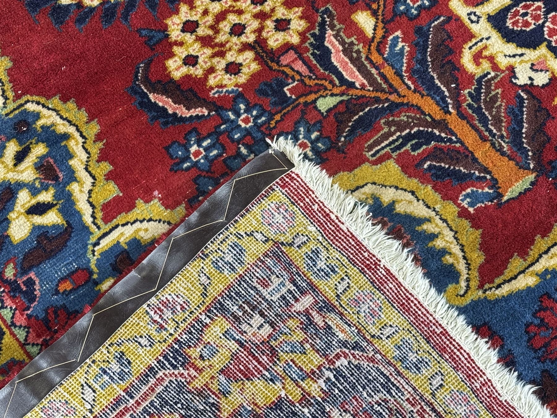 Mid-20th century Persian ground rug, featuring a bold red field and large lobed medallion, flanked by floral corner spandrels, enclosed within multiple borders of stylised vines and palmettes, with fringe to both ends