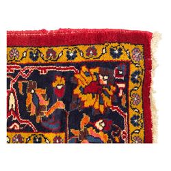 Mid-20th century Persian ground rug, featuring a bold red field and large lobed medallion, flanked by floral corner spandrels, enclosed within multiple borders of stylised vines and palmettes, with fringe to both ends
