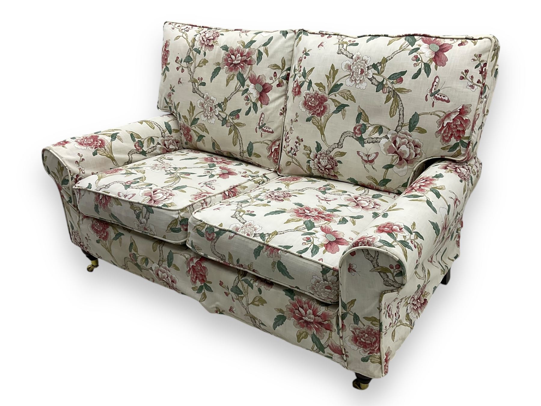 Steed Upholstery - 'Knightsbridge' two seater sofa, upholstered in cream fabric with pink and green floral design, loose back and seat cushions, raised on mahogany supports with brass castors
