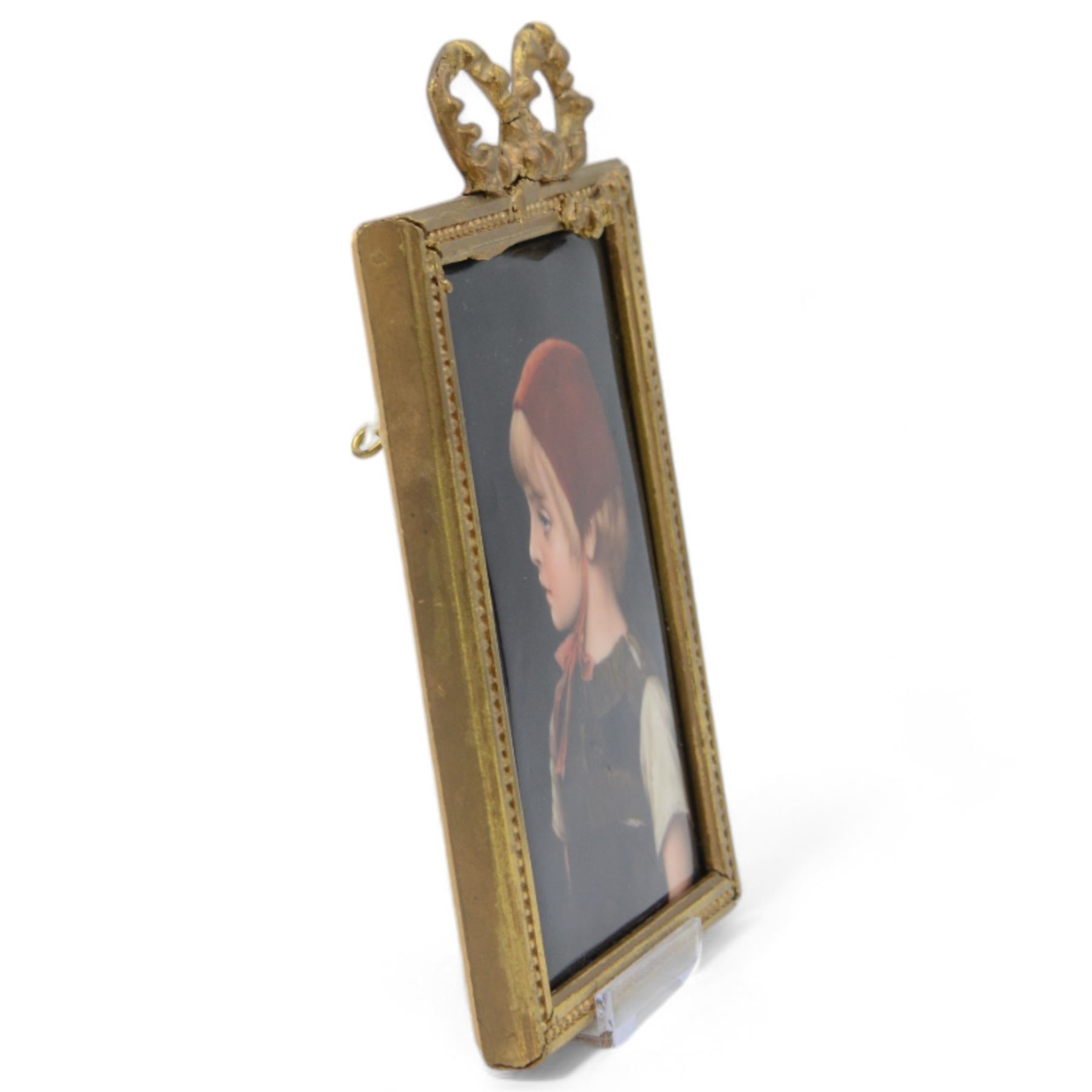 Late 19th/early 20th century German hand painted porcelain plaque, depicting a young girl in a red bonnet, after a painting by Gabriel Schachinger, within a beaded gilt frame with bow surmount, bearing paper label for Kunstinstitut fur Porzellan-Malerei Merkel-Heine Wiesbaden verso, and further paper label indistinctly inscribed '286 [...] Schachinger', also impressed 107, not including bow 16cm x 11.5cm
