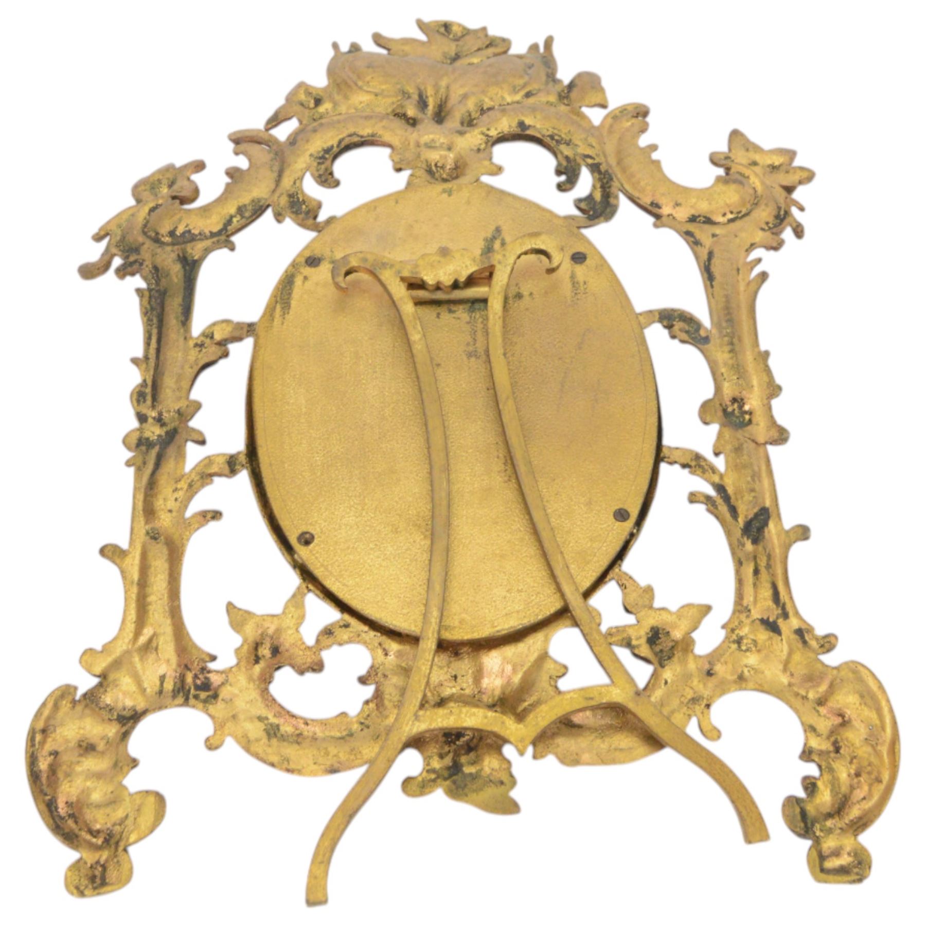 Rococo style cast gilt metal table mirror, the oval mirror plate within an open C scroll and foliate detailed frame, with easel style support verso, H33cm, together with a pair of cast gilt metal acanthus surround frames, H28.5cm