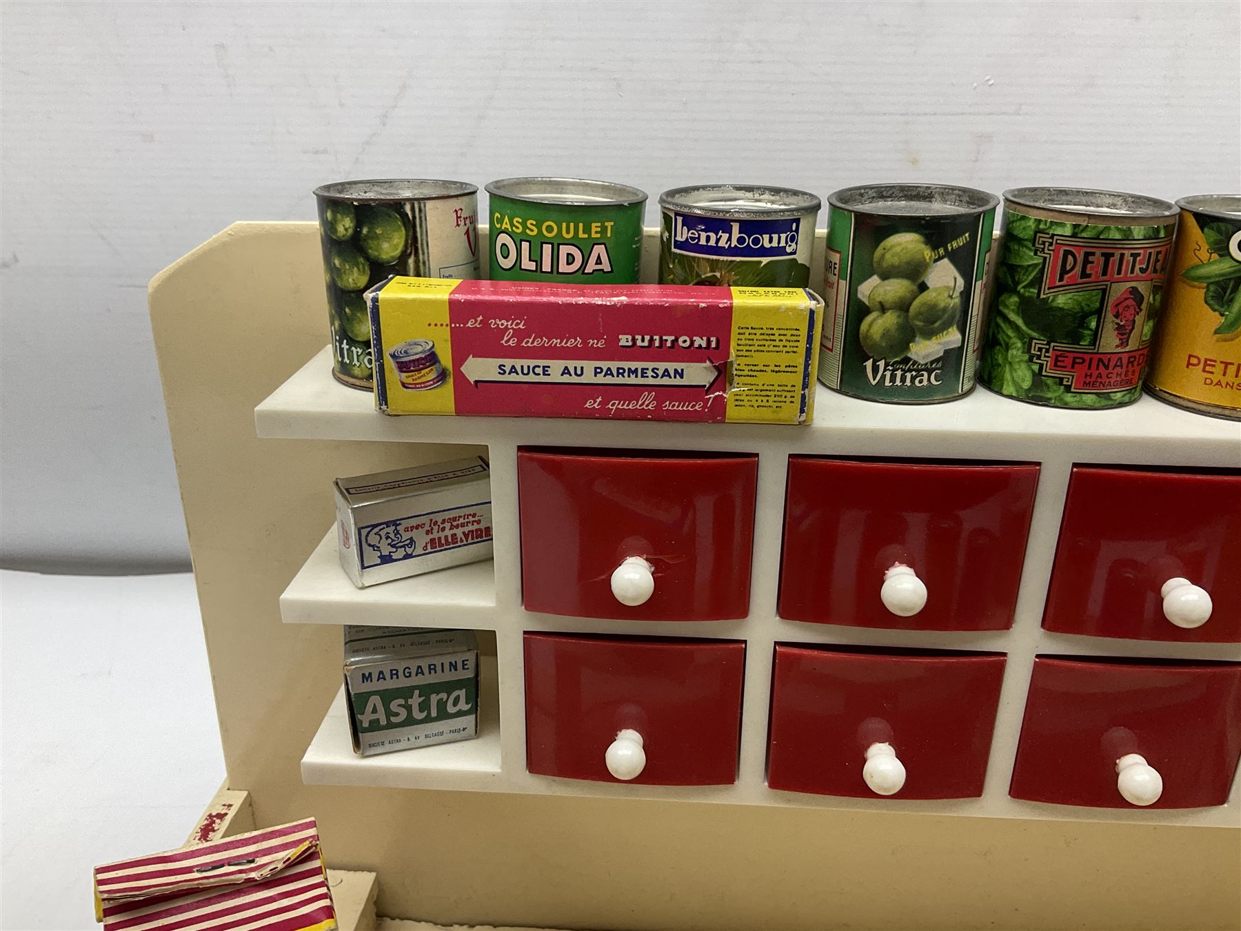 Late 1950s continental red and white painted wooden diorama of a grocery shop interior with fitted shelves and drawers and freestanding 'glazed' counter, fully stocked with miniature tin cans and packets of food L42cm H23cm D22cm