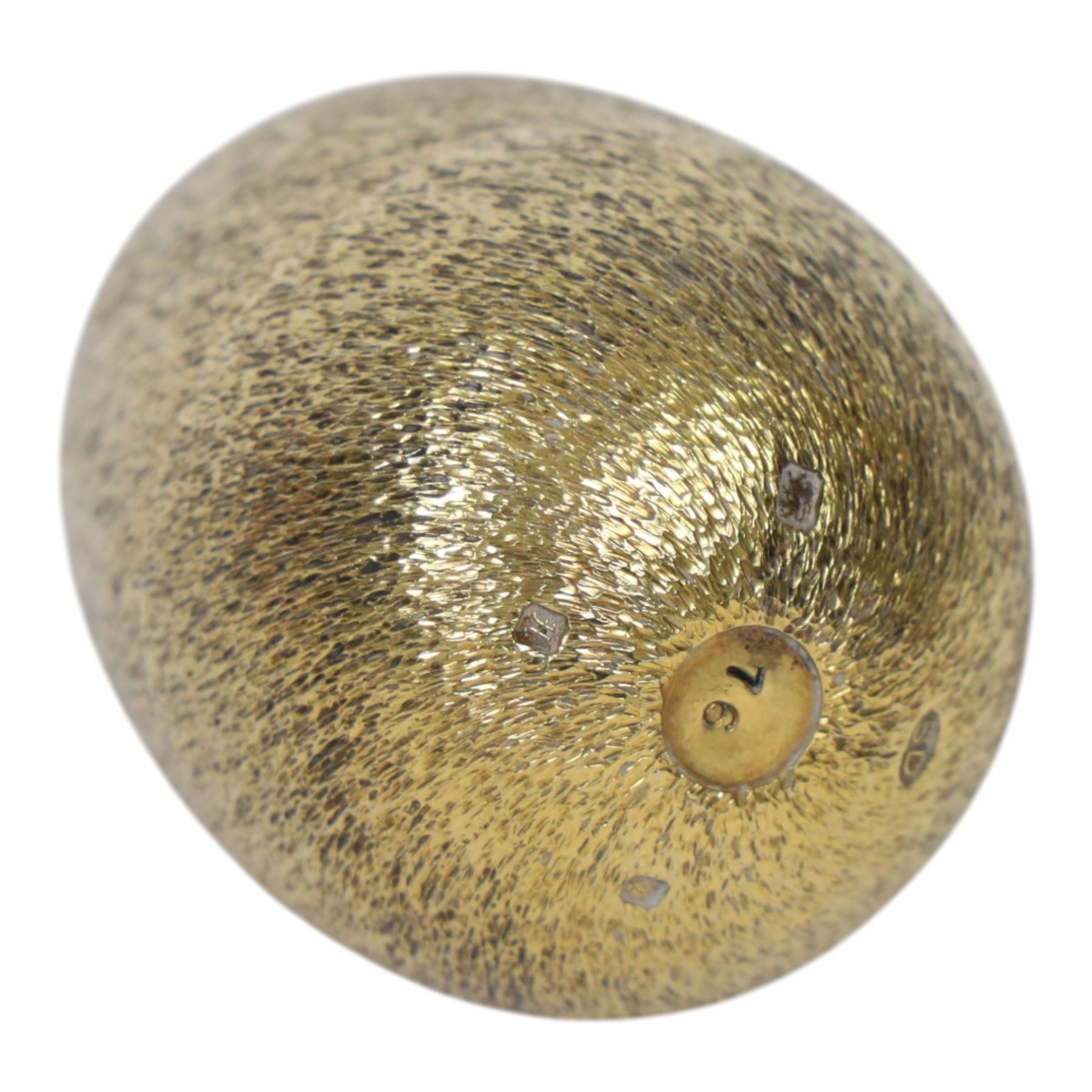 Late 20th century silver and silver-gilt surprise egg, the textured gilt exterior opening to reveal a clutch of chicks, the clustered heads supported upon a spring, within a jagged and lobed silver and gilt encasement, with green enamel surround, hallmarked Stuart Devlin, London 1982, H7cm