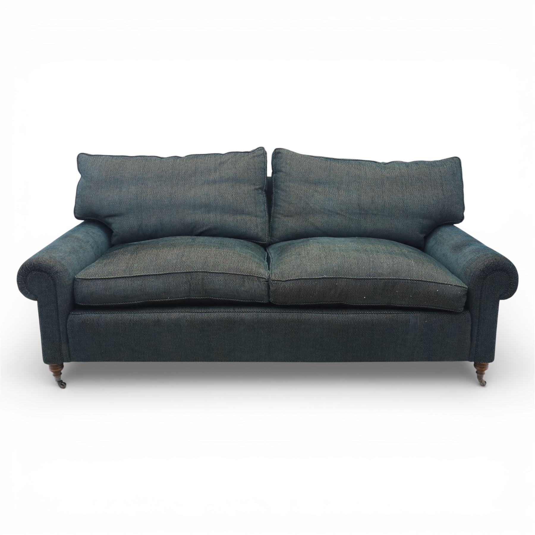 Late 20th century three seat sofa upholstered in green fabric, with gently rounded scroll arms, loose seat and back cushions, raised on turned wooden legs with castors, rear splayed legs