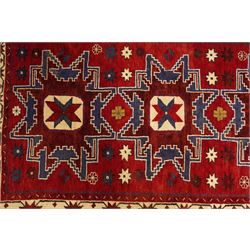 Caucasian Kazak hand-knotted rug, madder red ground with three large stepped geometric medallions in dark blue, ivory and red, surrounded by stylised star and flowerhead motifs, enclosed by ivory border with repeating eight-pointed stars, fringed ends