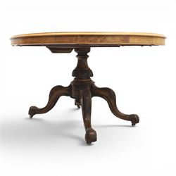 Victorian figured walnut oval loo tilt top table, raised on a heavily carved quatriform base with scrolled supports, terminating in castors