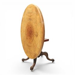 Victorian figured walnut oval loo tilt top table, raised on a heavily carved quatriform base with scrolled supports, terminating in castors