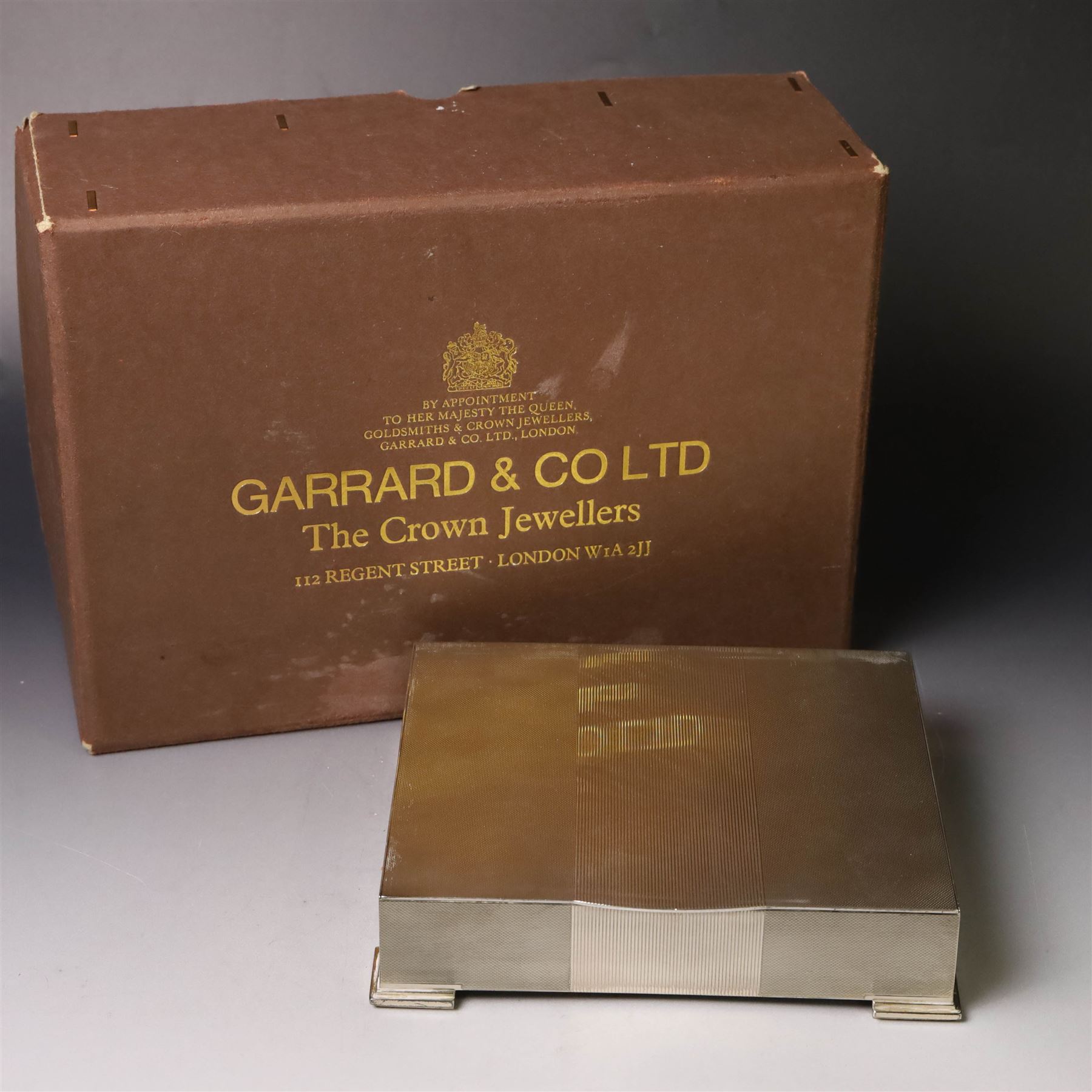 1960s silver mounted cigarette box, of rectangular form with engine turned decoration, upon four bracket feet, with presentation engraving to interior lid reading  'British Aircraft Corporation (Operating) Limited Commemorating the Queen's Award to Industry 1967, hallmarked James Geraghty, Birmingham 1965, with retailers mark for Asprey, W16.5cm, H4.5cm, in Garrard & Co Jewellers box