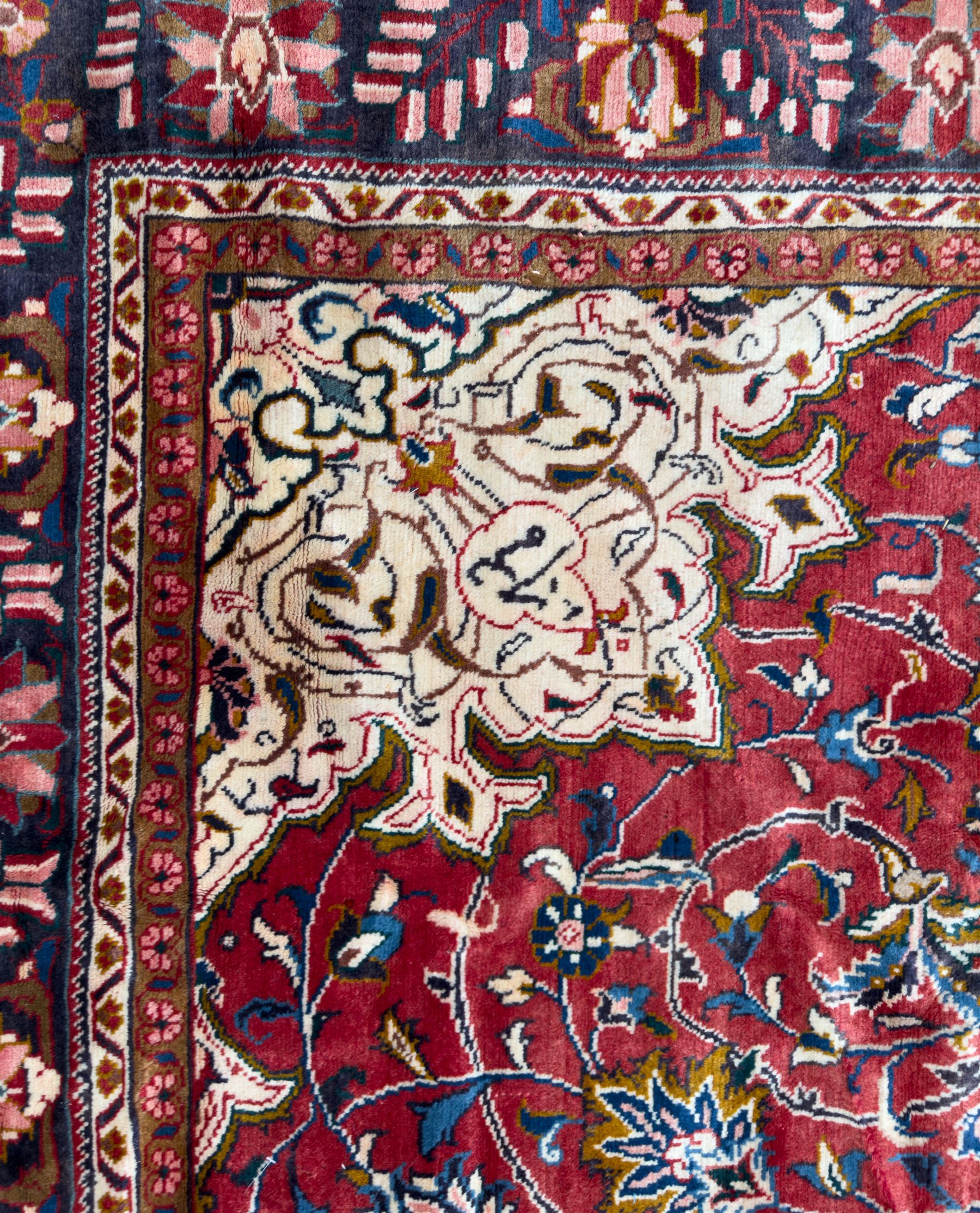 Northwestern Persian Lillihan hand-knotted carpet, madder red field with scrolling vines, rosettes, and palmettes around a central circular medallion in navy, ivory and ochre, and ivory ground spandrels within a navy border of stylized flowerheads and vines between multiple guard stripes 
