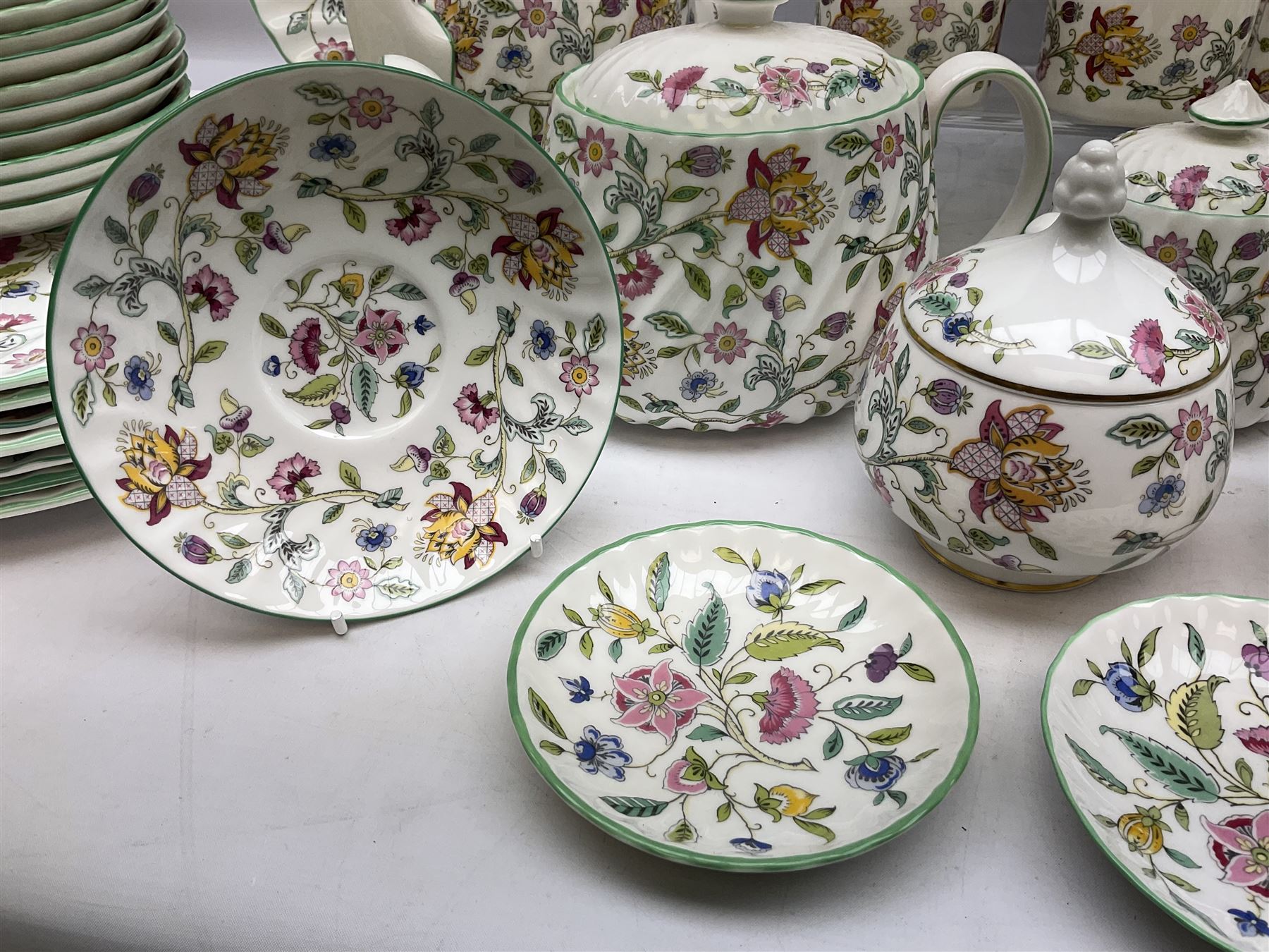 Minton Haddon Hall pattern tea and dinner wares, including basket dish, two covered tureens, six dinner plates, eight dessert plates, twelve tea plates, six soup bowls, six cereal bowls, teapot, coffee pot, milk jug, covered sucrier twelve tea cups and saucers, six mugs, footed bon bon dish, pair of candlestick holders, cake knife and slice etc (81)